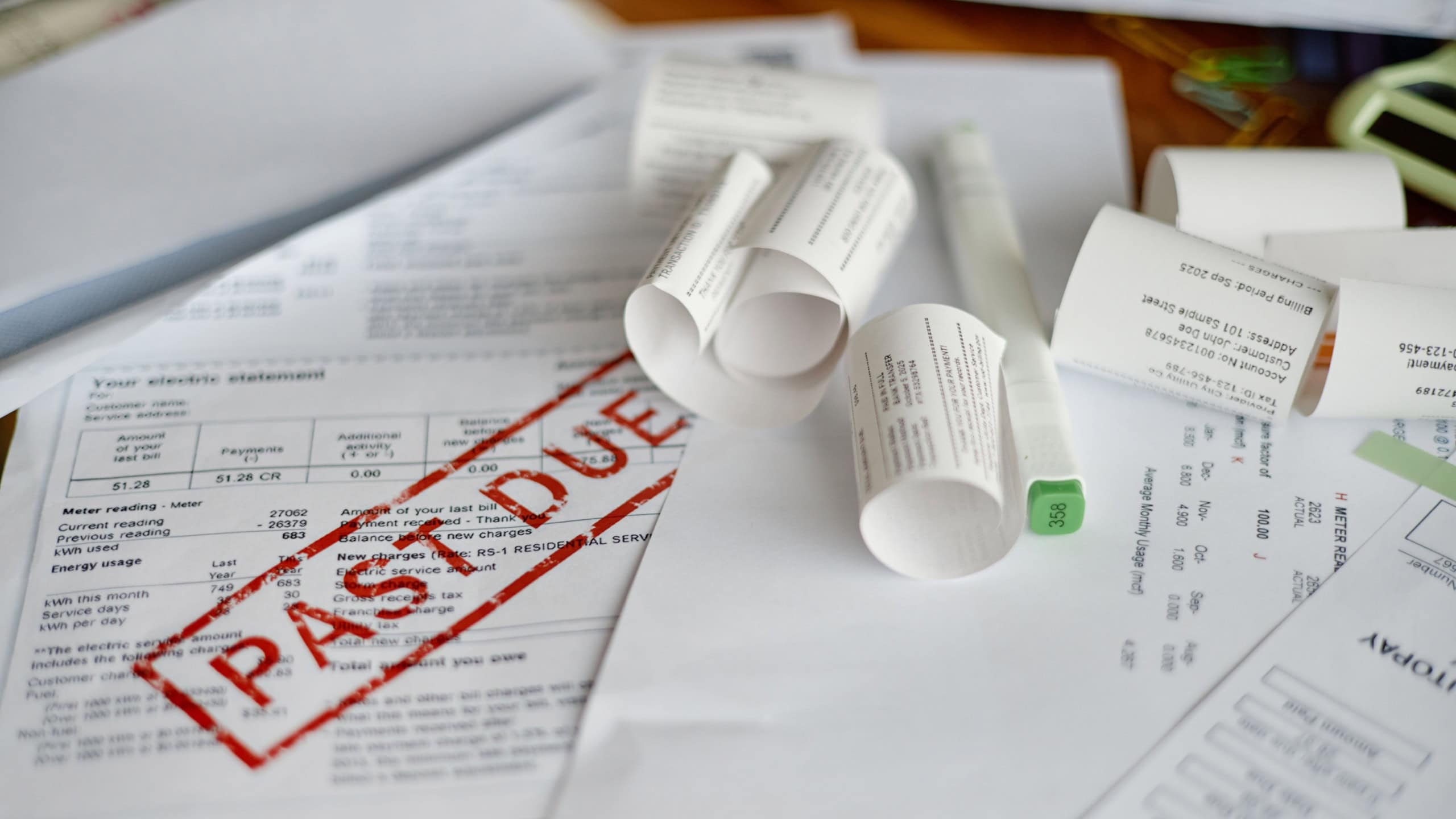 Closeup showing multiple utility bills and invoices scattered on desk, including electric statement marked past due, emphasizing financial analysis and overdue payment context