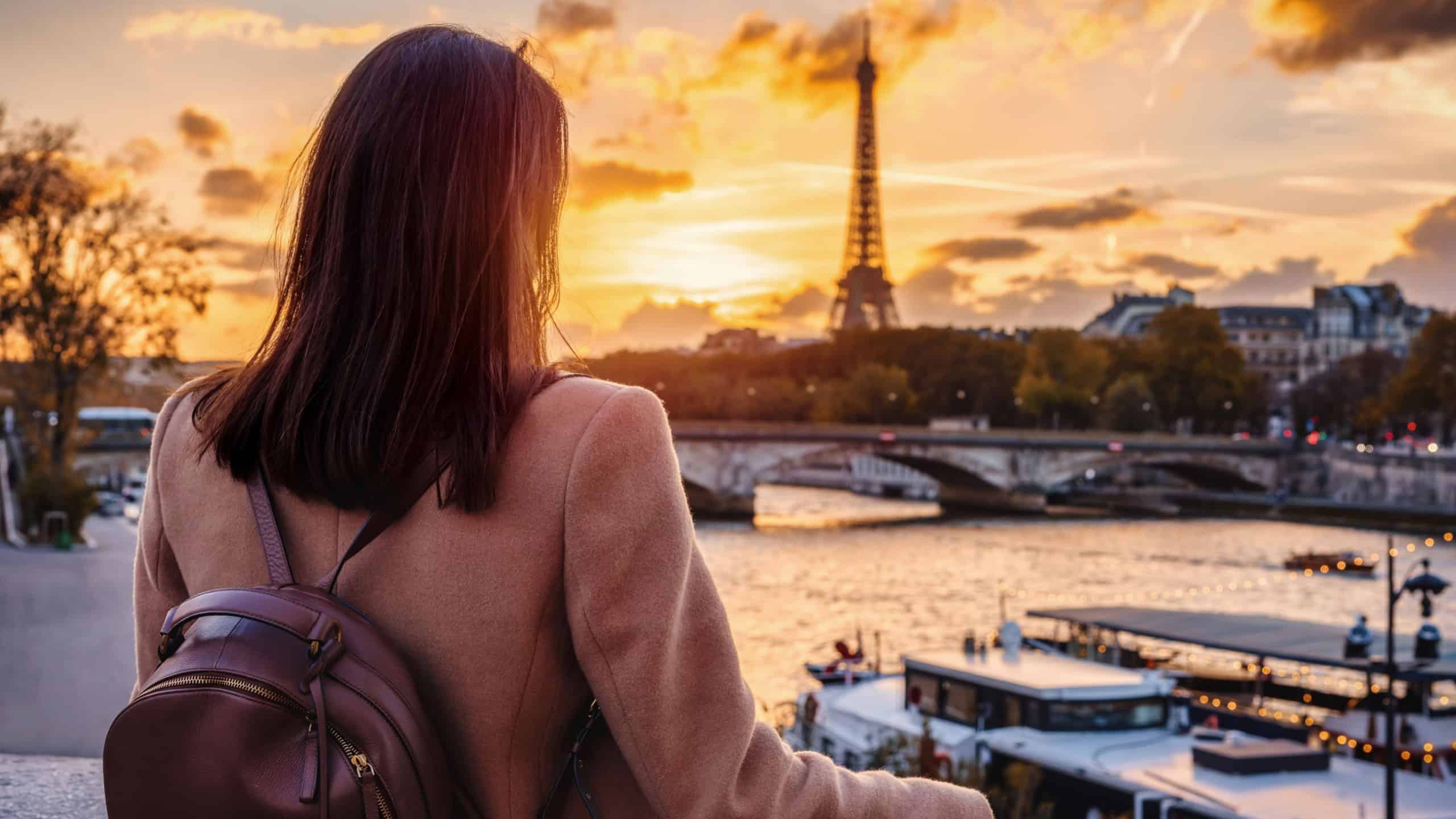 A tourist woman on a sightseeing city trip looks at the beautiful sunset view of Paris, France