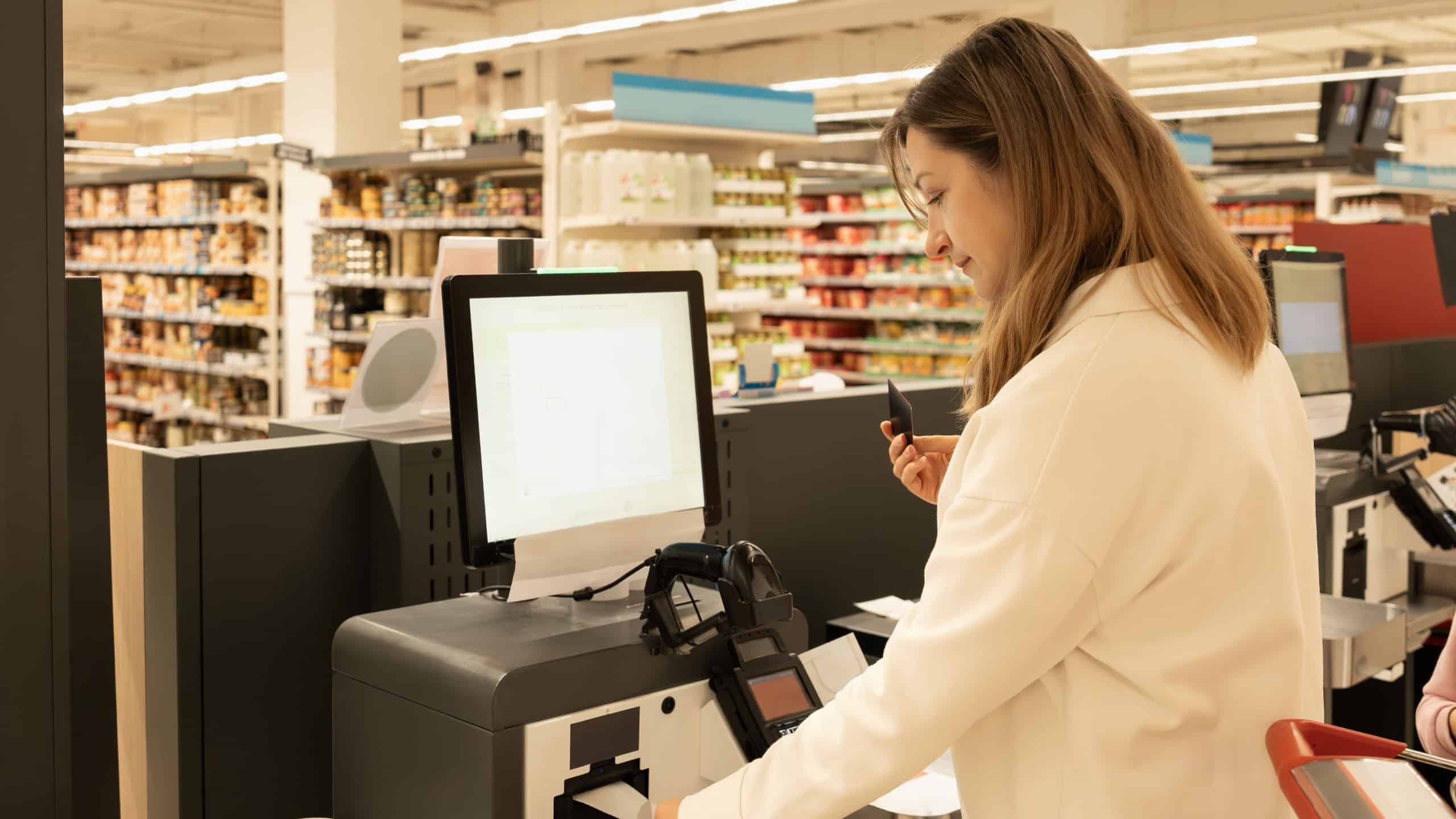 A woman pays with a credit card at a self-service checkout in a supermarket