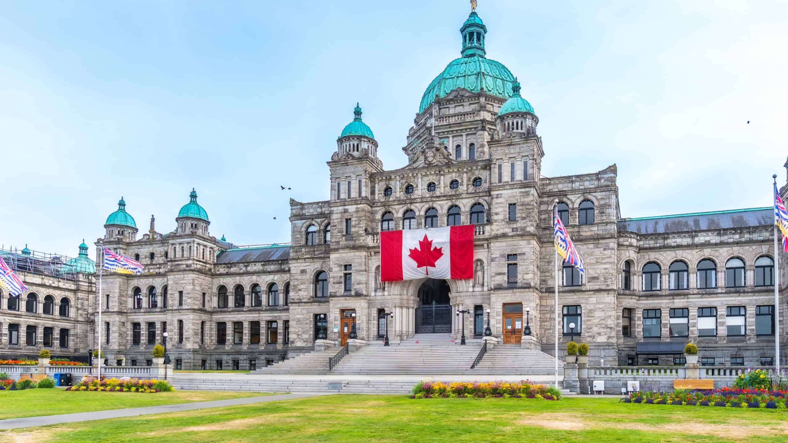 British columbia parliament buildings with large canadian flag hanging from the front during a sunny summer day in victoria, british columbia