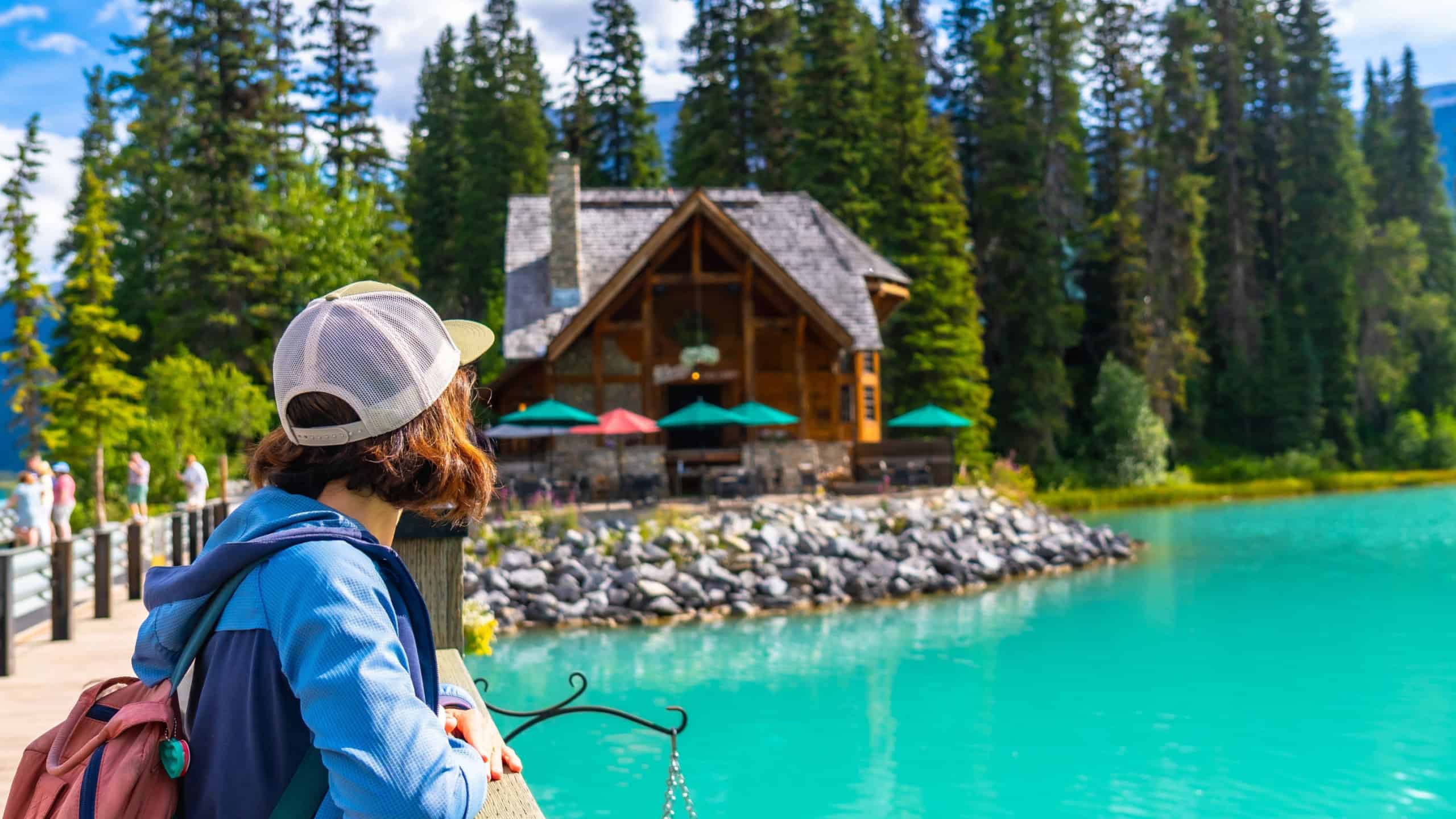 Female hiker admiring the turquoise waters of emerald lake and its charming lodge, nestled among lush pine forests in banff national park, alberta, canada