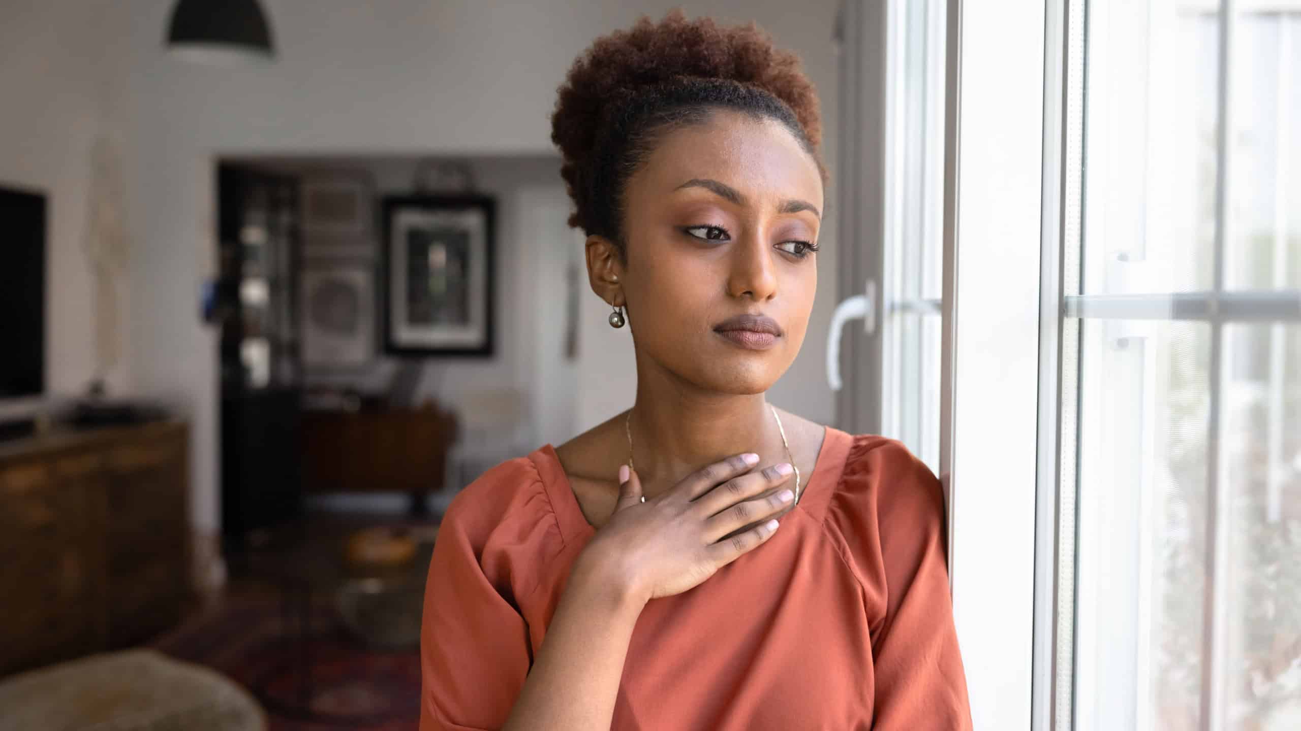 Thoughtful serious young African woman looking out of window in deep sad thoughts, thinking on problems, bad news, personal troubles, feeling depressed, frustrated