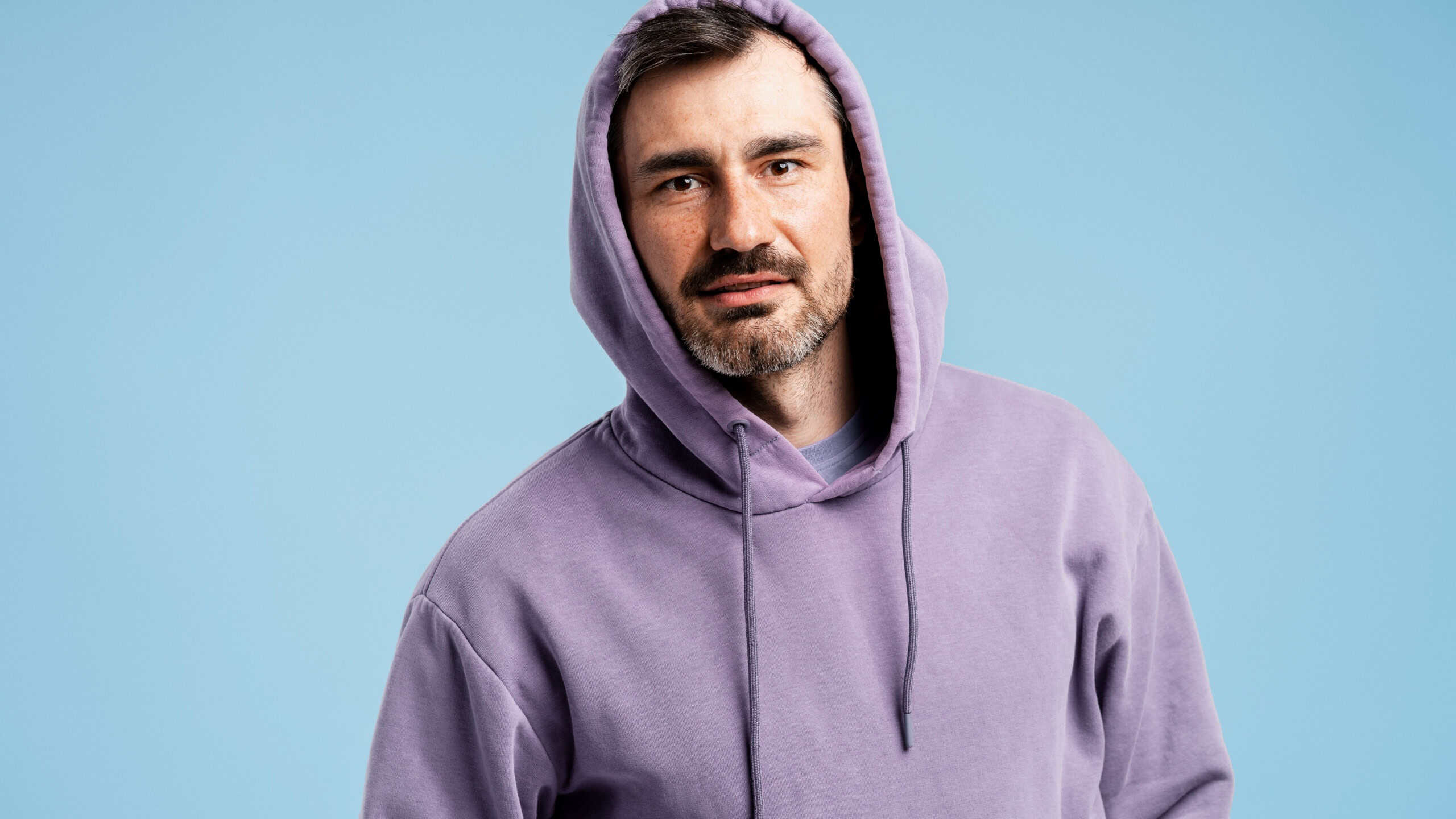 Adult male wearing hooded sweatshirt, looking at camera in a studio setting