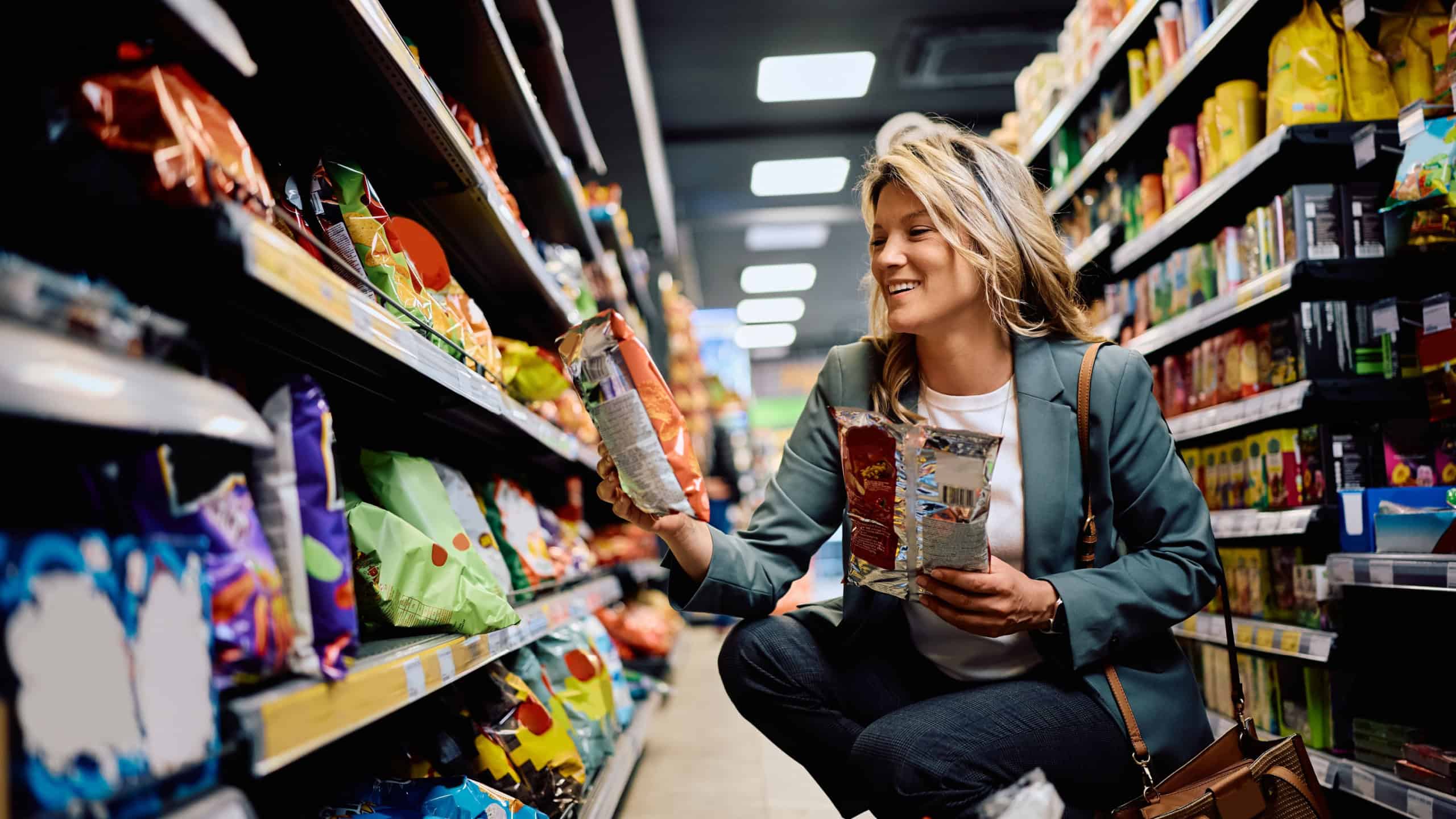 Happy woman taking snacks from a shelf while buying groceries in supermarket. 