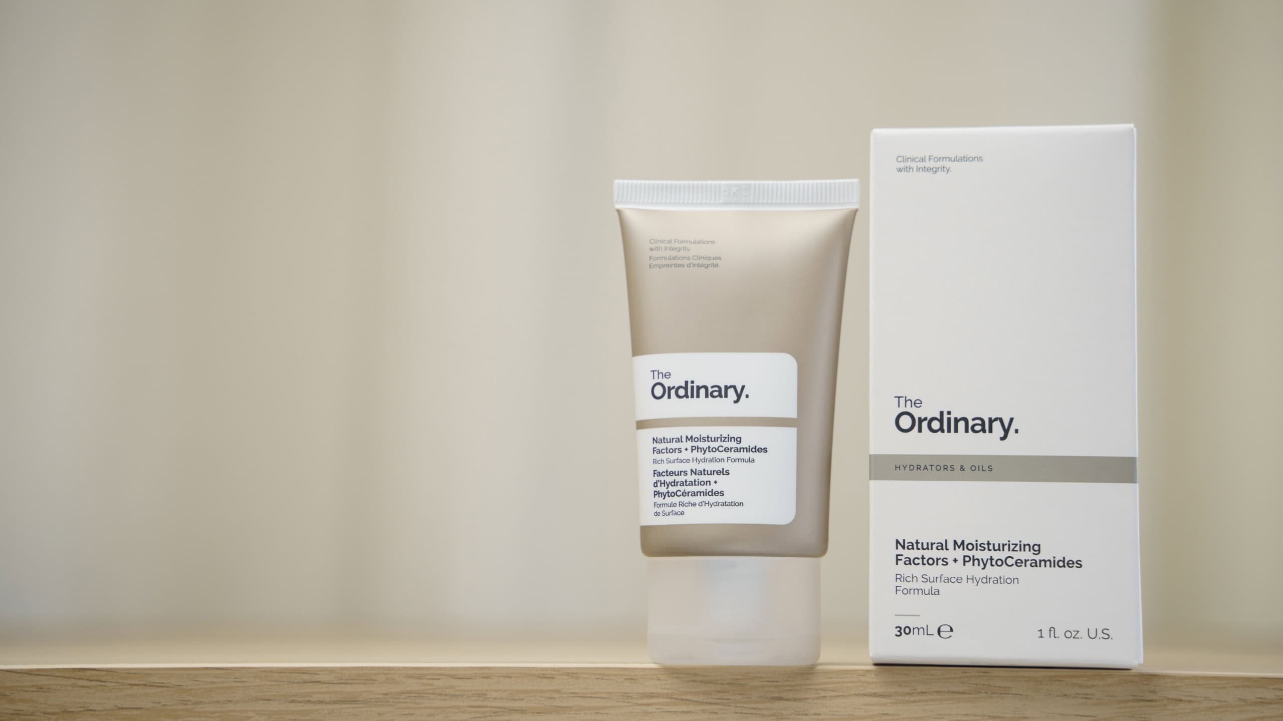 Minimalist product shot of The Ordinary Natural Moisturizing Factors PhytoCeramides face moisturizer tube and packaging on a wooden shelf, clean beauty branding