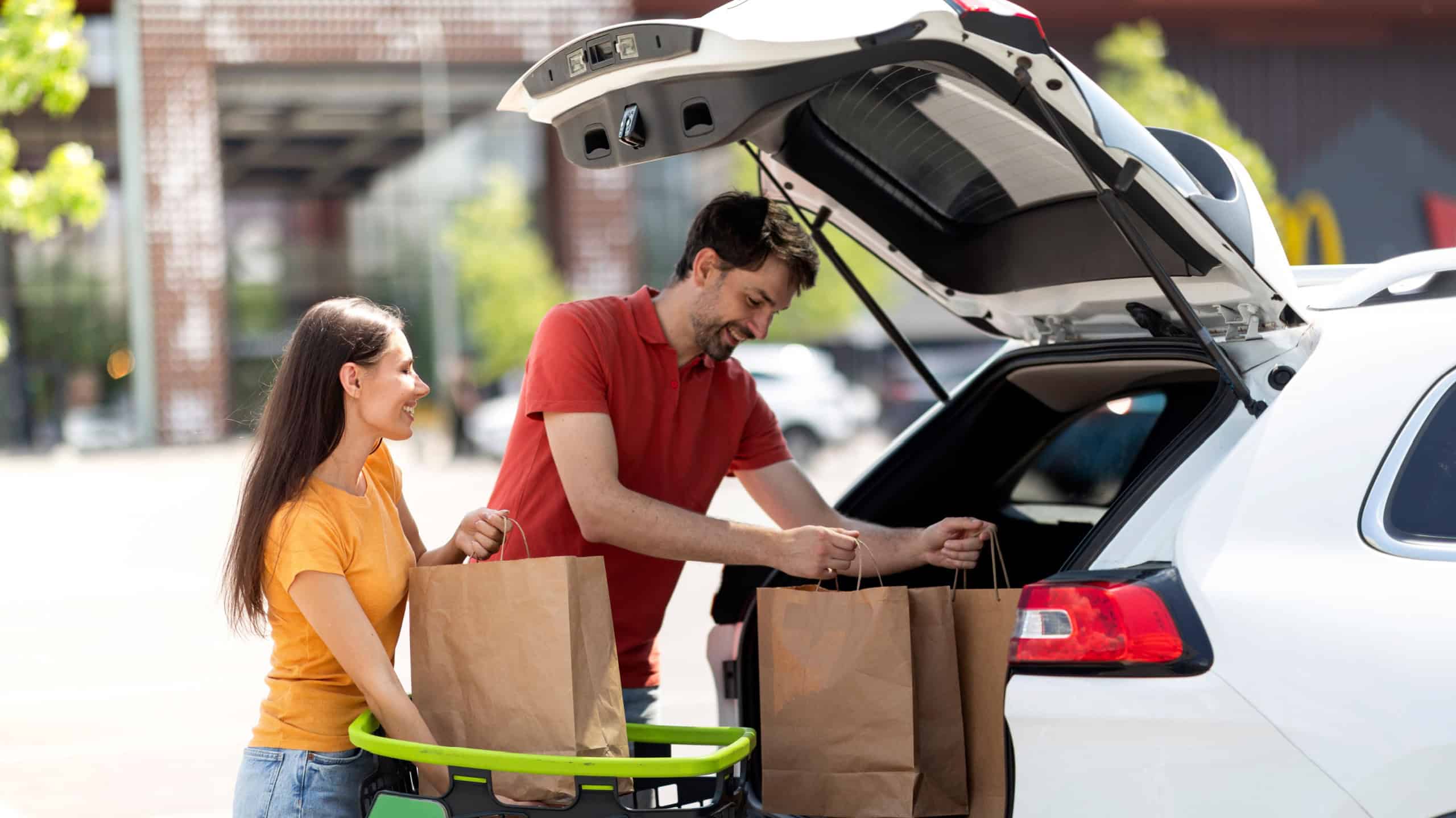 Couple buying food in grocery store, packing purchases in car
