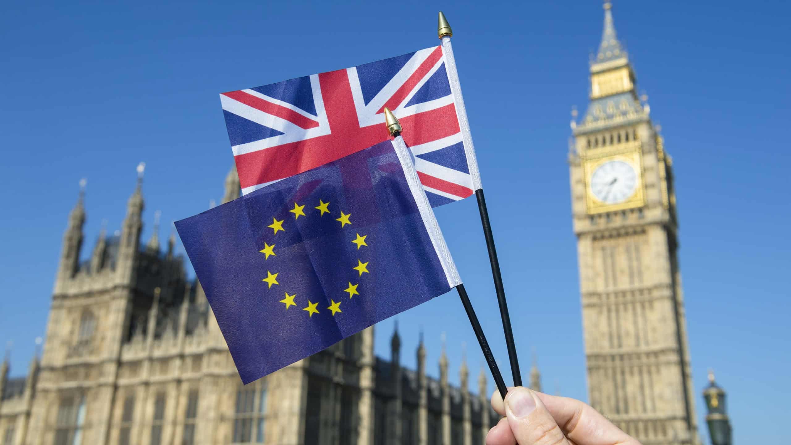 Hand waving European Union and British Union Jack flag in front of Big Ben and the Houses of Parliament at Westminster Palace, London as the Brexit process moves ahead
