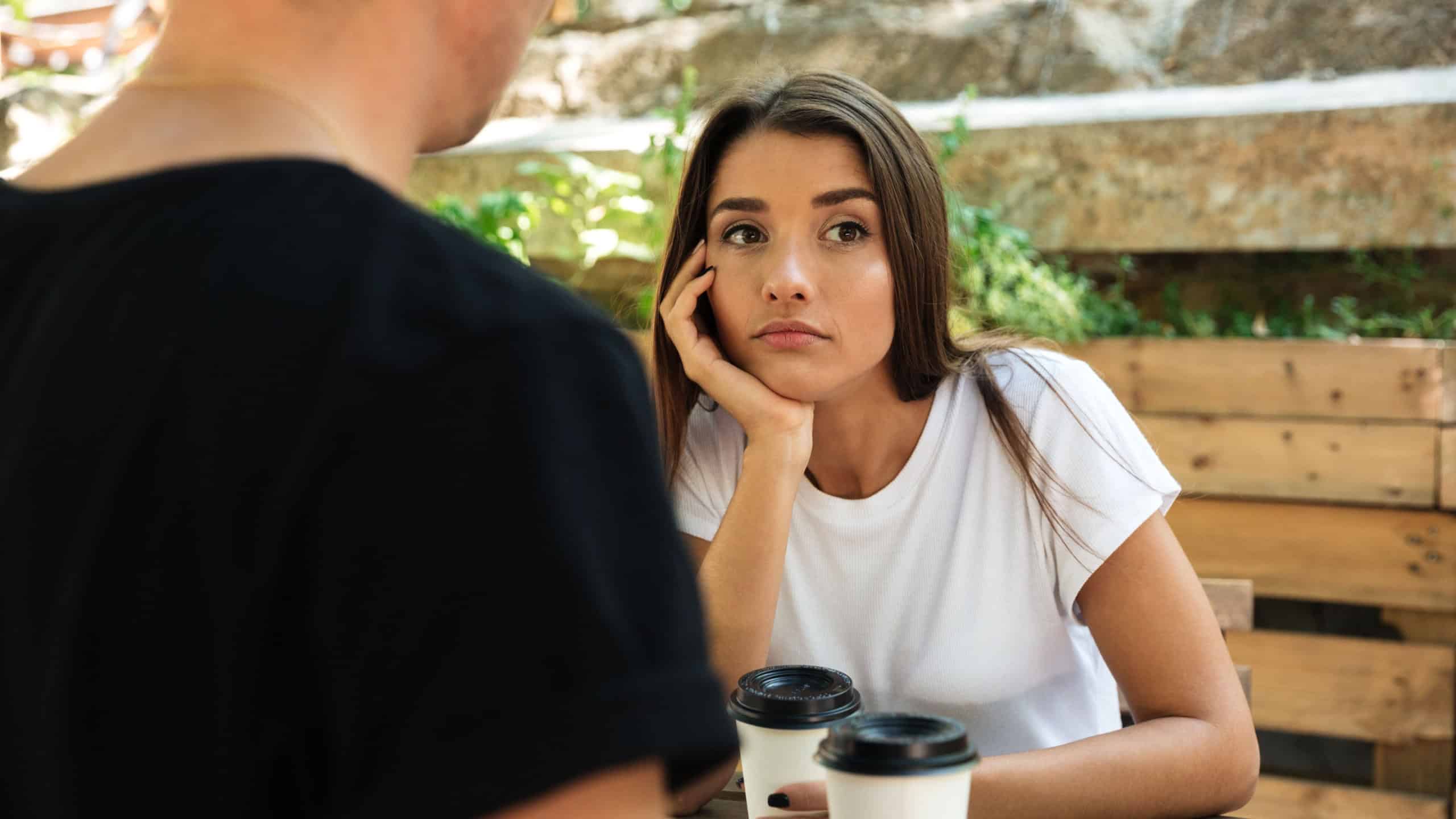 Young bored girl sitting and drinking coffee with her boyfriend at a cafe outdoors