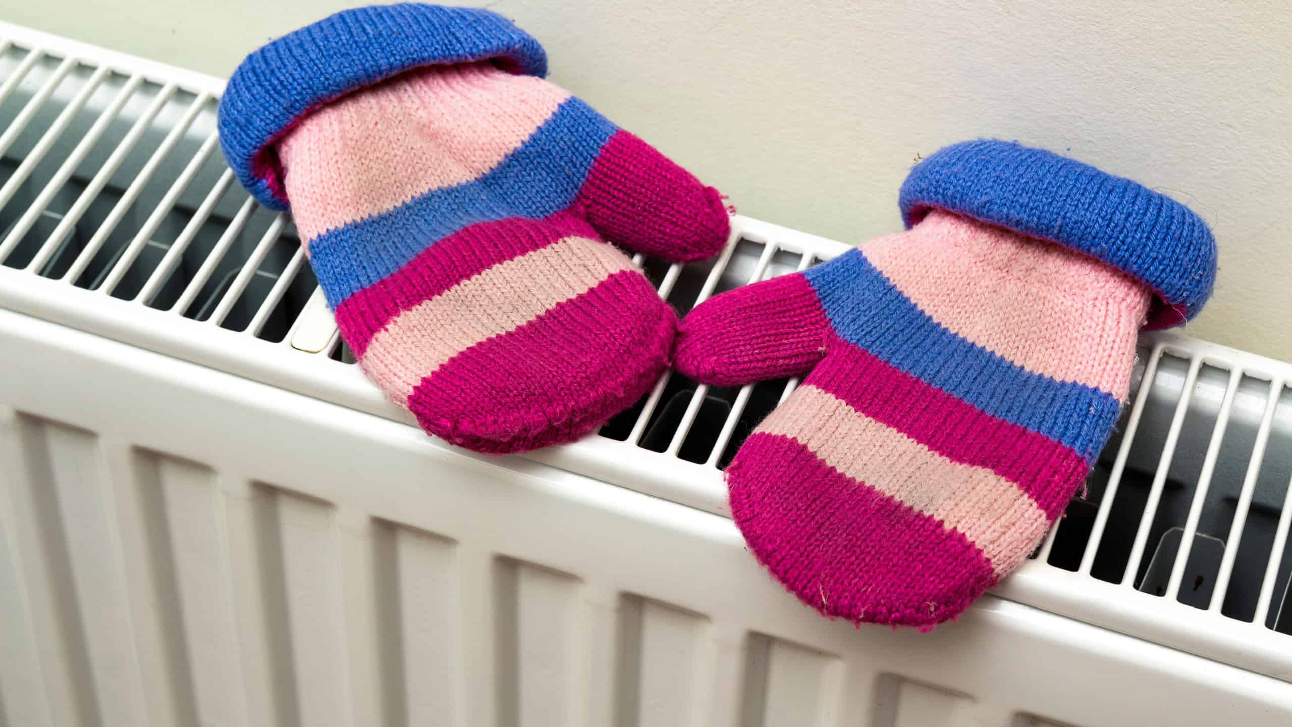 Children's warm hand knitted striped woolen gloves drying on heating radiator after winter day outside