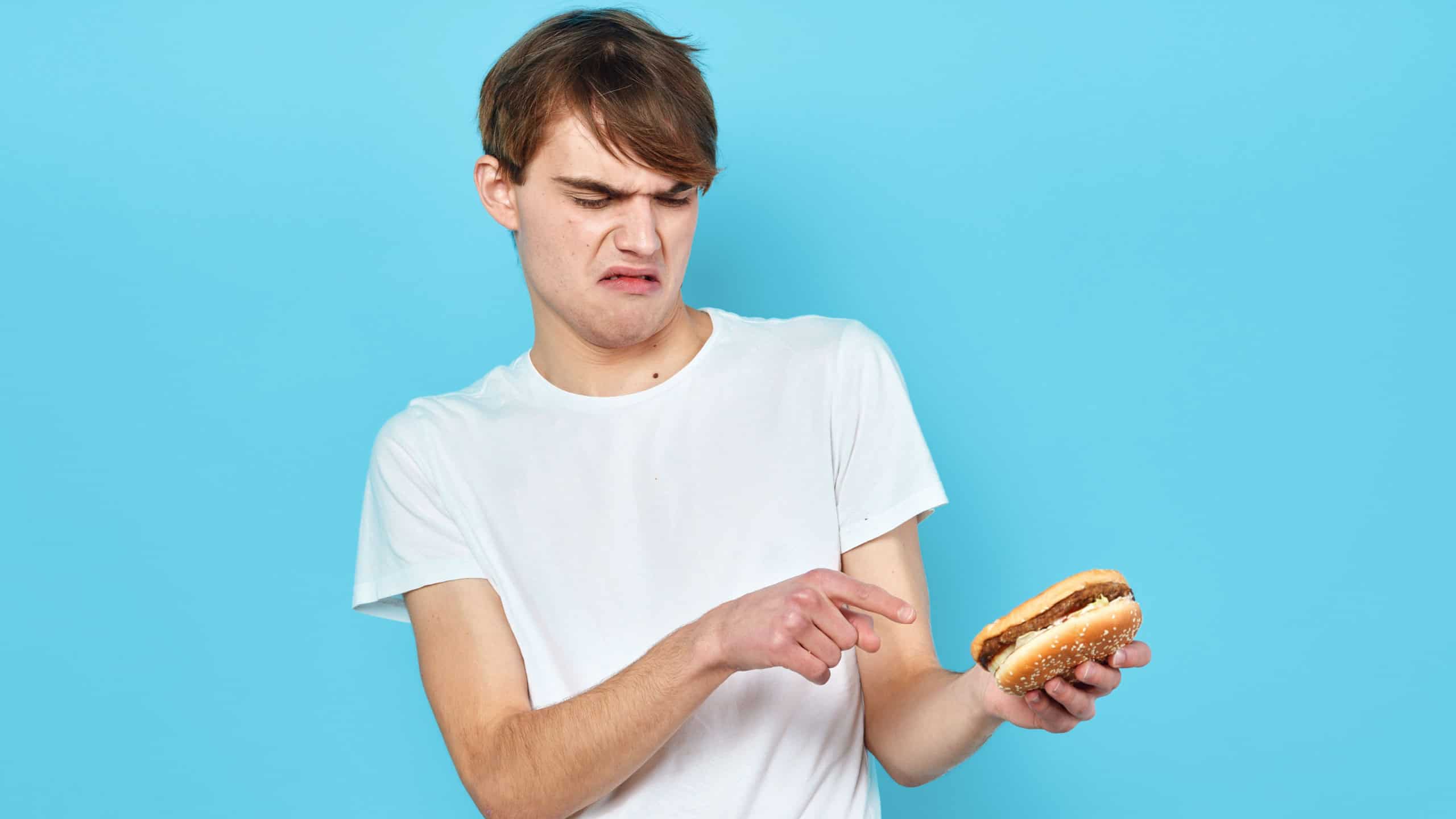 A man with disgust looks at a cheeseburger on a blue background fast food