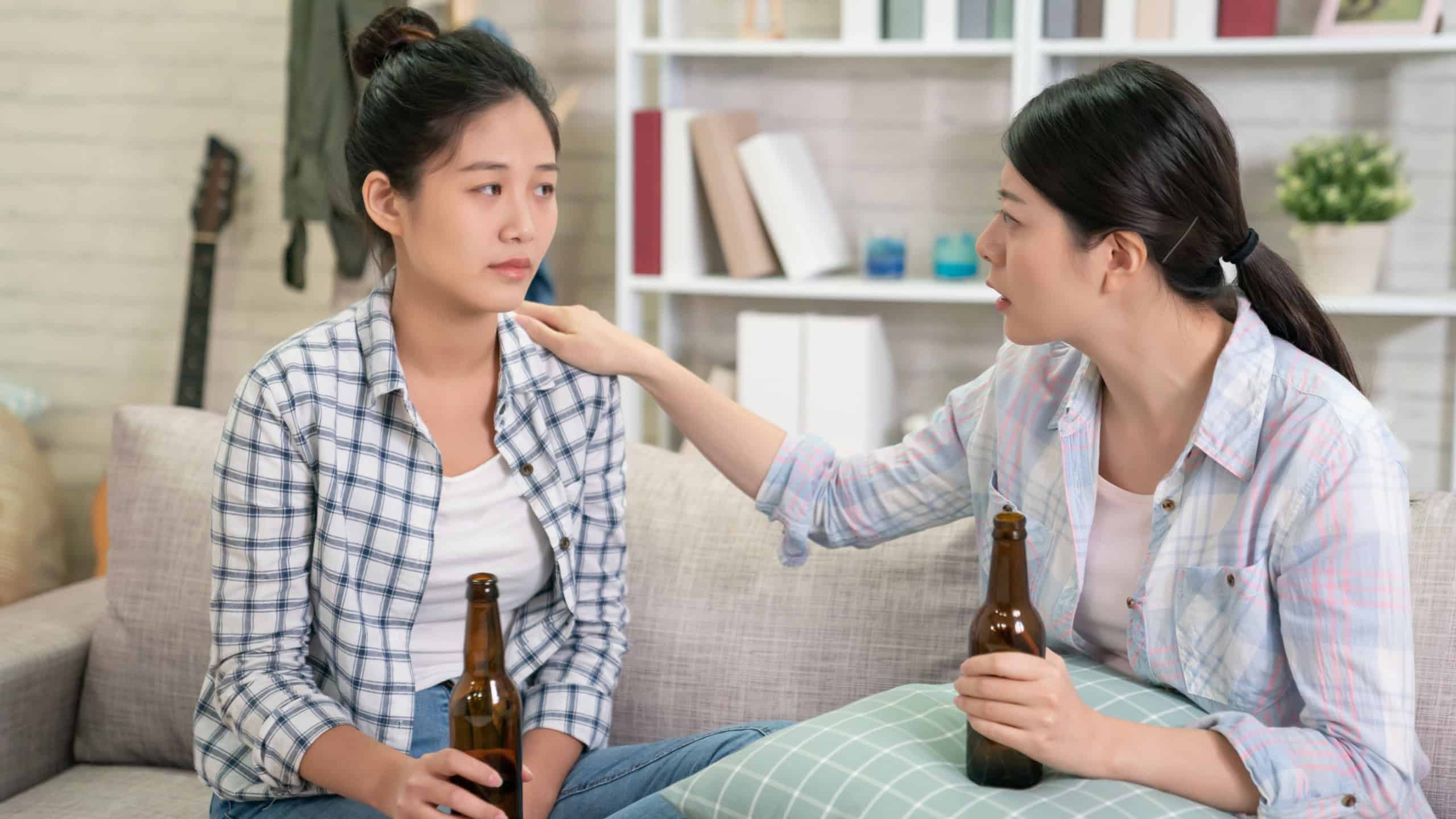 Woman comforting to sad depressed friend who needs help. Depression with alcohol concept. stressed upset young girl with unhappy face holding beer bottle looking at her best sister touching shoulder