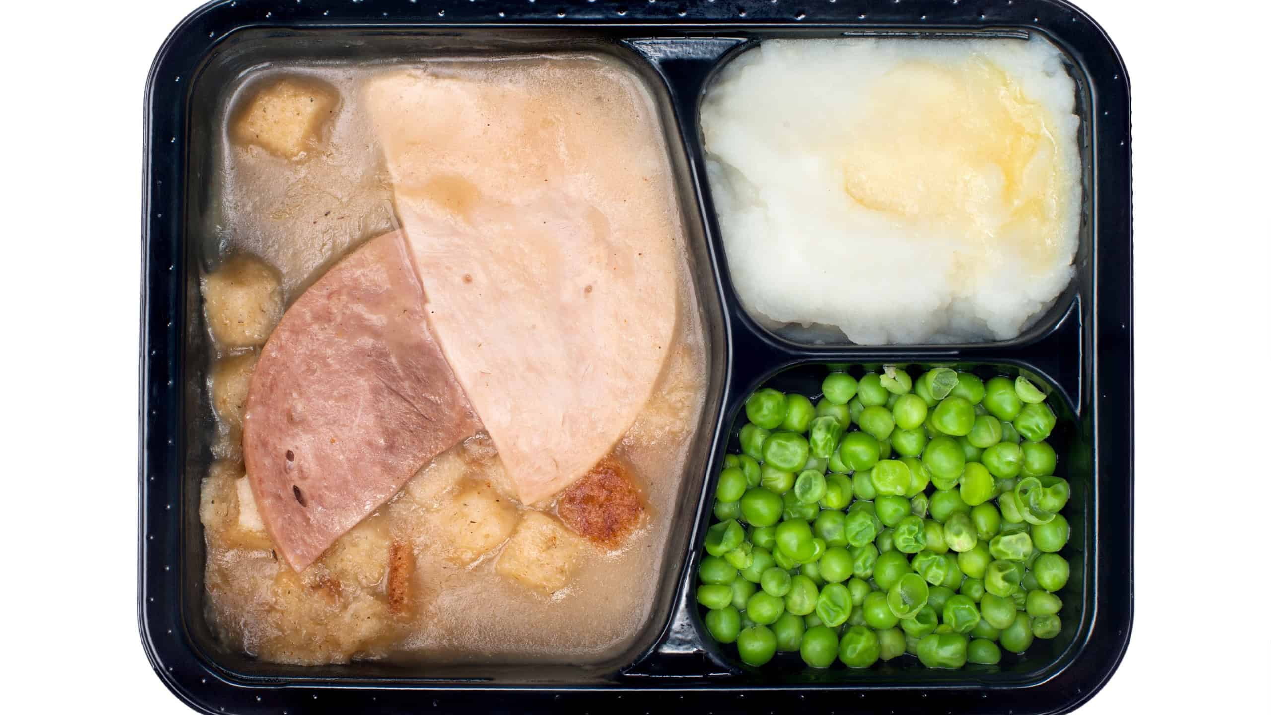 A frozen dinner consisting of turkey, ham, peas and mashed potatoes isolated on white