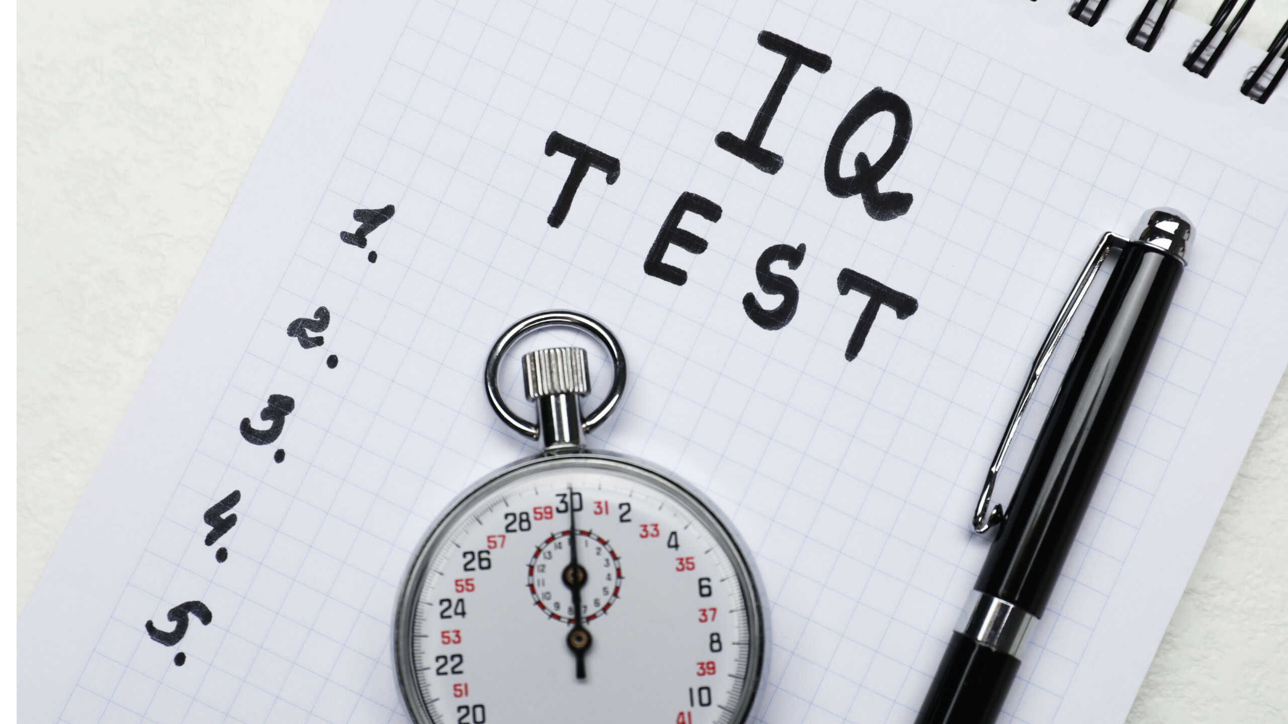 Notebook with words IQ Test, pen and timer on white table, top view