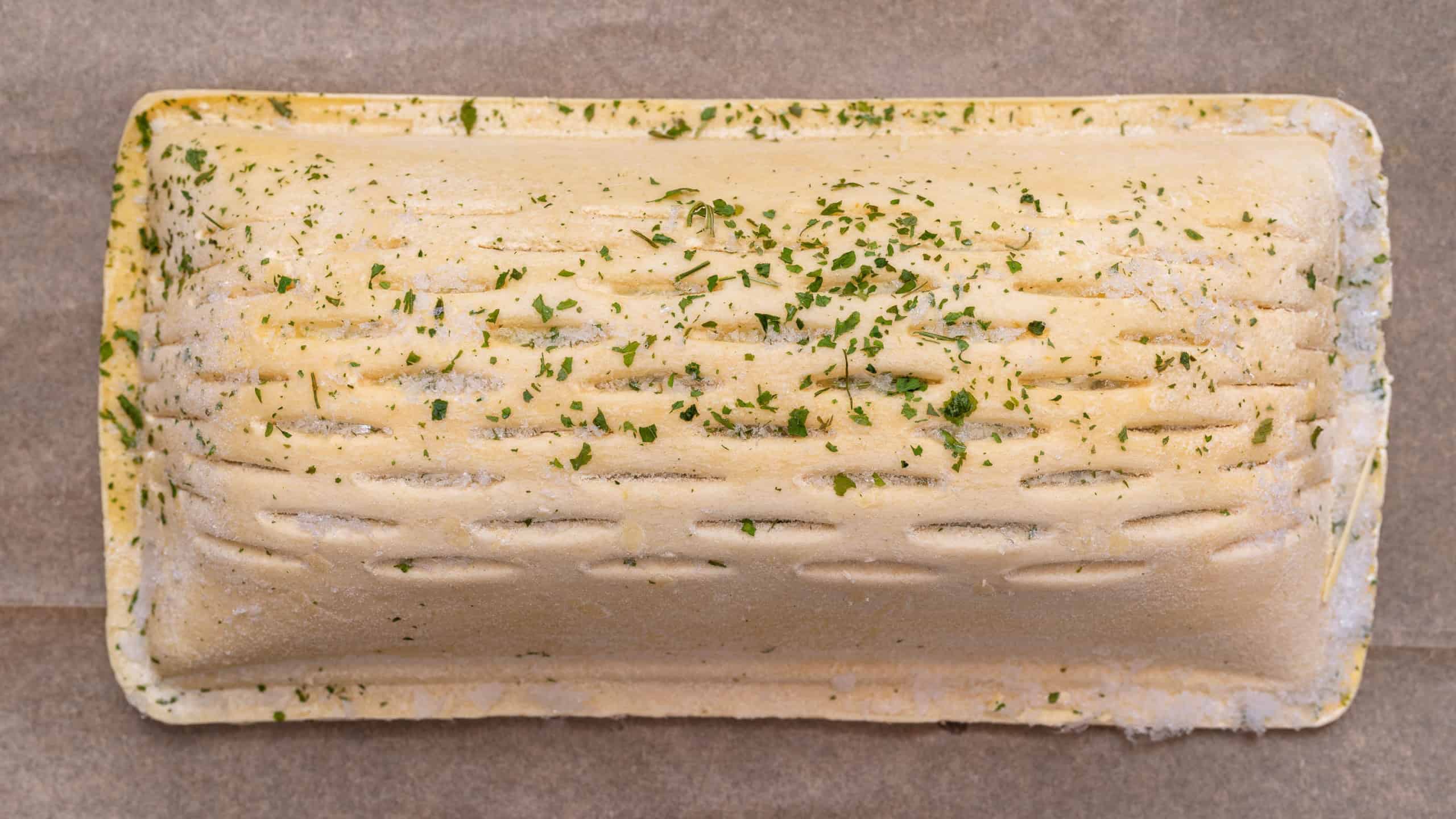 Frozen puff pastry with salmon lying on baking paper, isolated on a brown background top view.