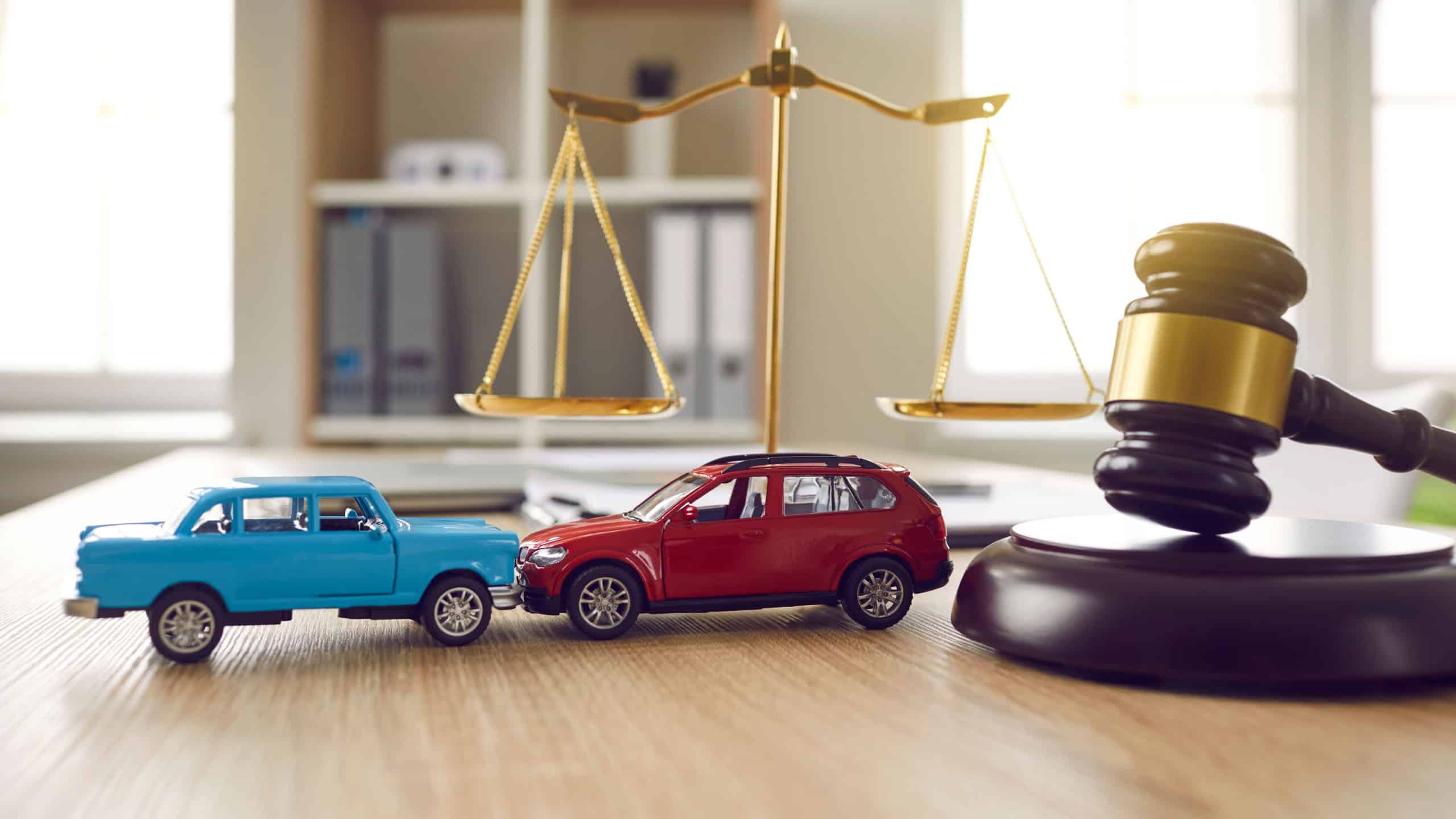 Two small cars on table in courtroom. Gavel and little toy car models on desk in courthouse. Road crash, law, justice, lawyer services, civil trial, accident case study, insurance coverage concept