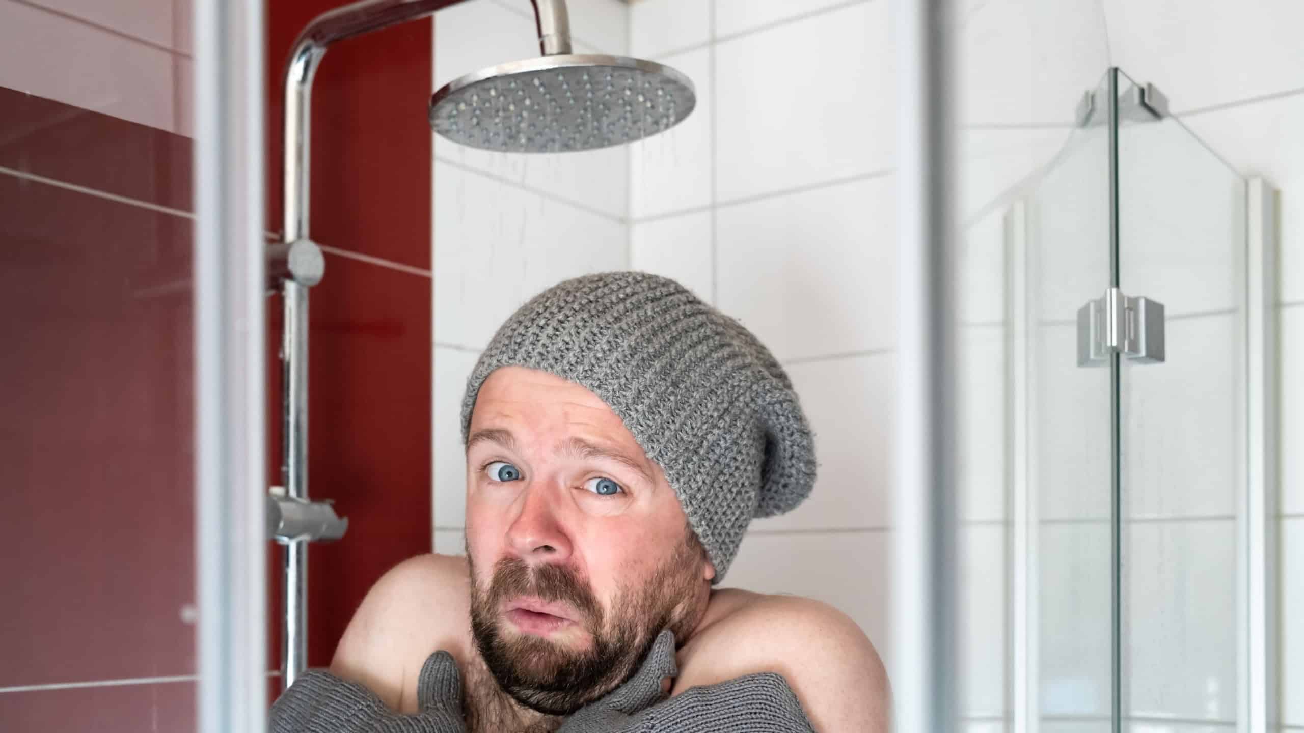 Man in a hat and mittens in the shower under cool water. Concept of energy crisis and savings.