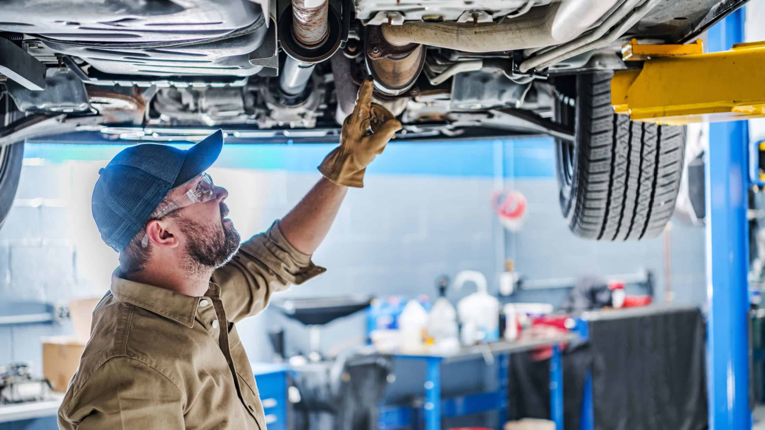 Professional Caucasian Mechanic Standing Under the Vehicle Lifted on Car Lift Checking the Condition of Catalytic Converter. Automotive Theme.