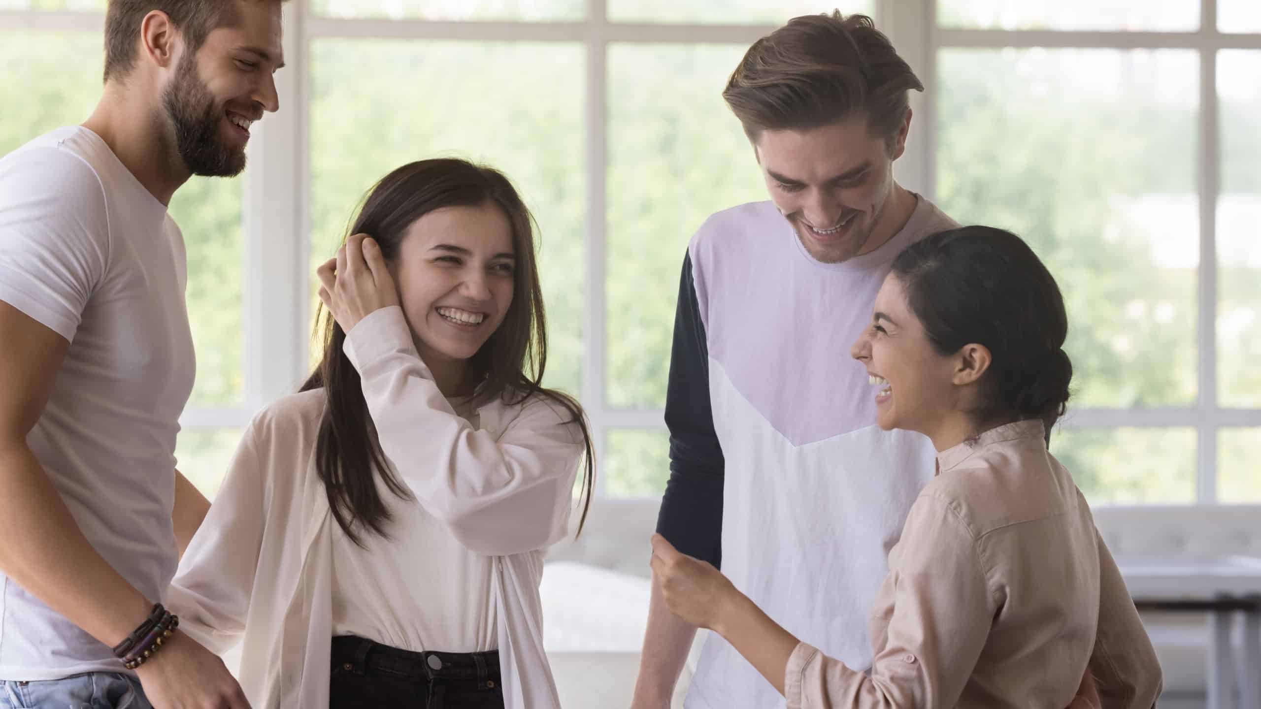 Diverse group of friends standing in cafe interior, chatting, talking, laughing, having fun. Multiethnic couples enjoying leisure, communication, double date, hugging