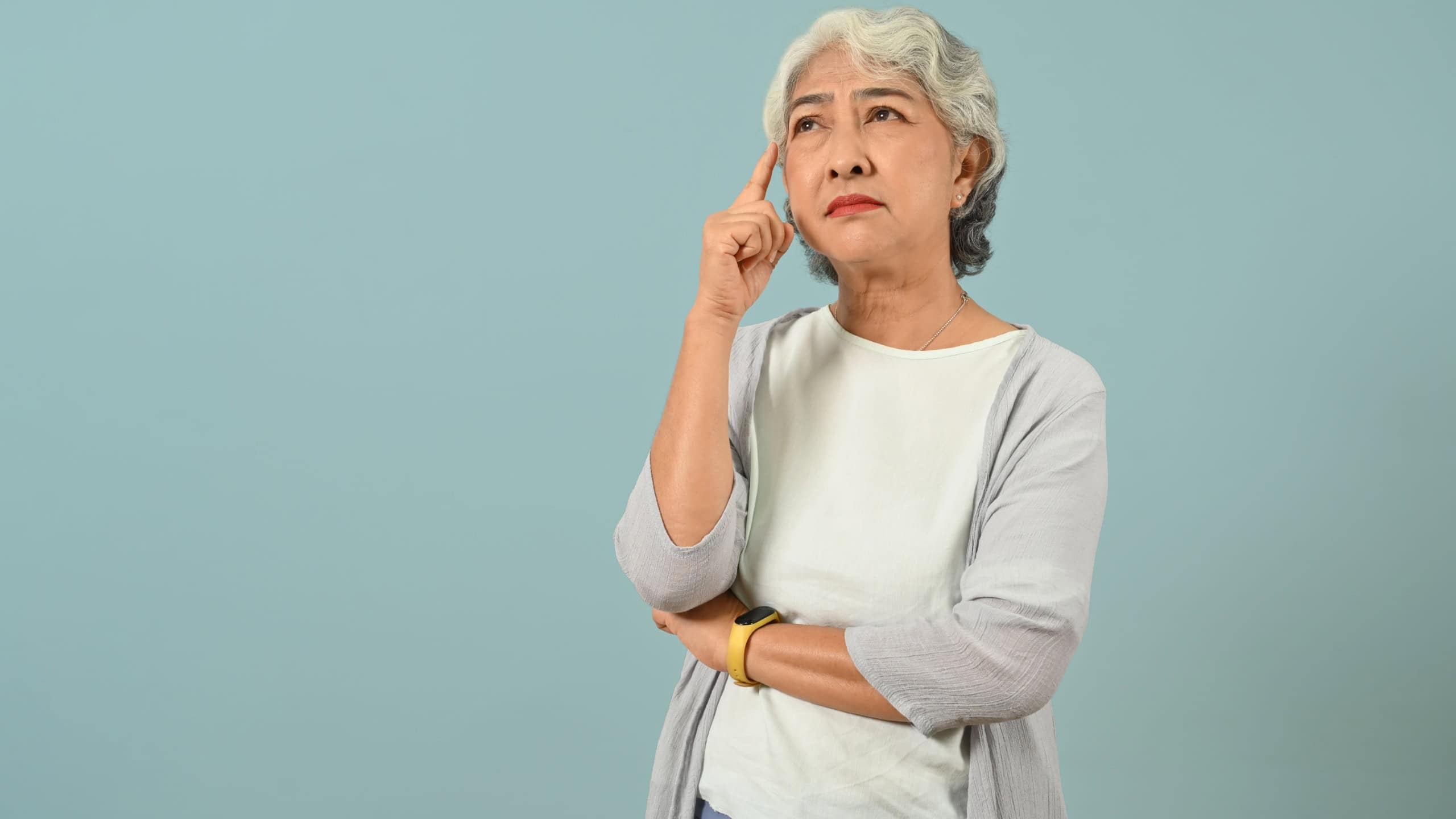 Confused and thoughtful senior woman thinking and looking up expressing doubt and wonder isolated blue background