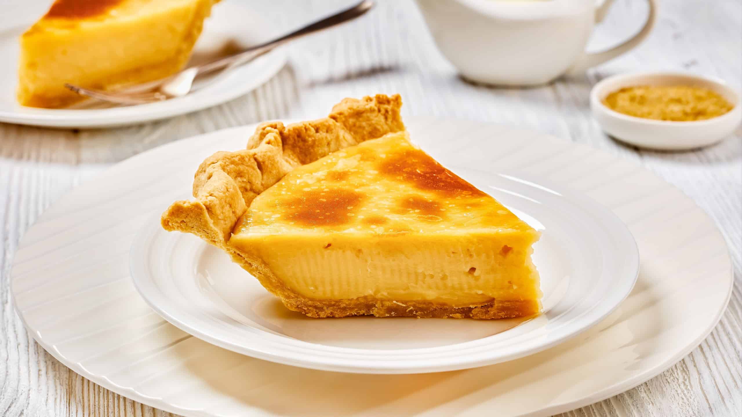 a slice of classic sugar cream pie, hoosier pie, indiana custard cream pie on white plate on white wood table
