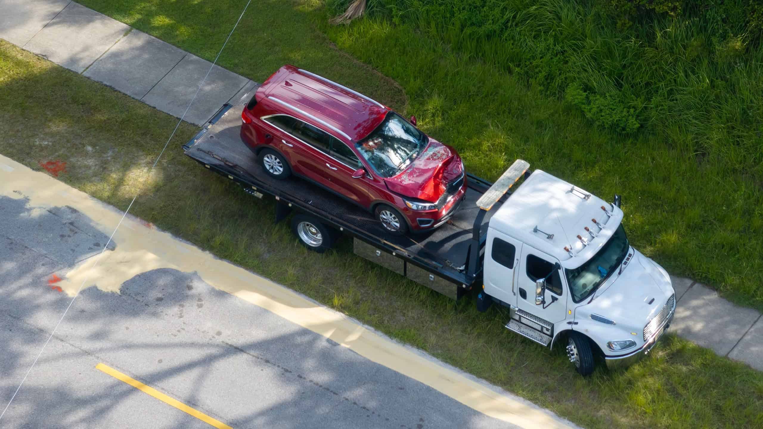 Tow truck hauling smashed vehicle on car accident site. Emergency services personnel responding to traffic crash on American street. First responders helping on road in the USA