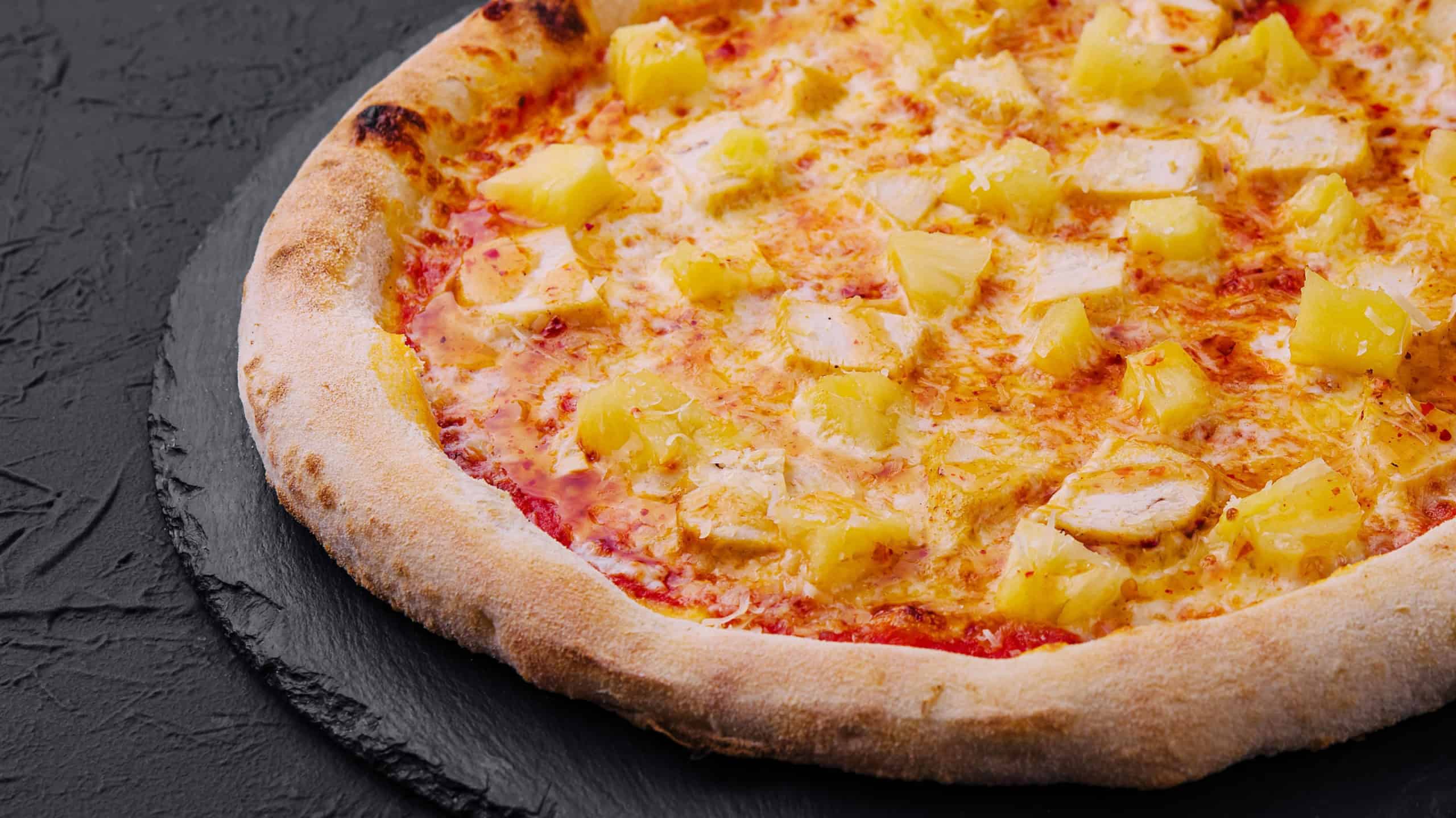 Close-up of a hawaiian pizza with pineapple and ham toppings on a dark background