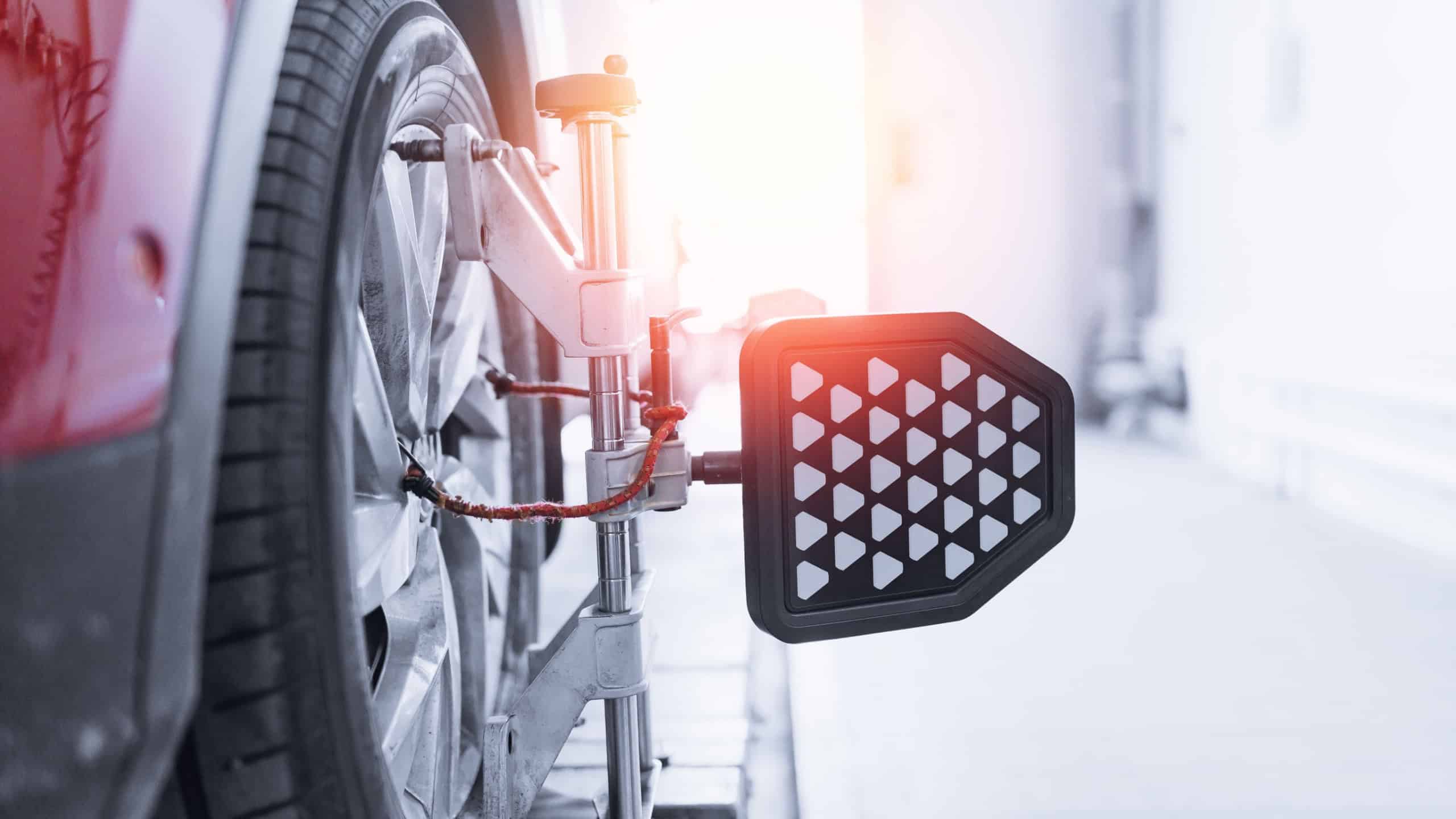 Vehicle inside garage workshop for auto camber fixing work. Closeup car wheel alignment on stand with sensors check in service station