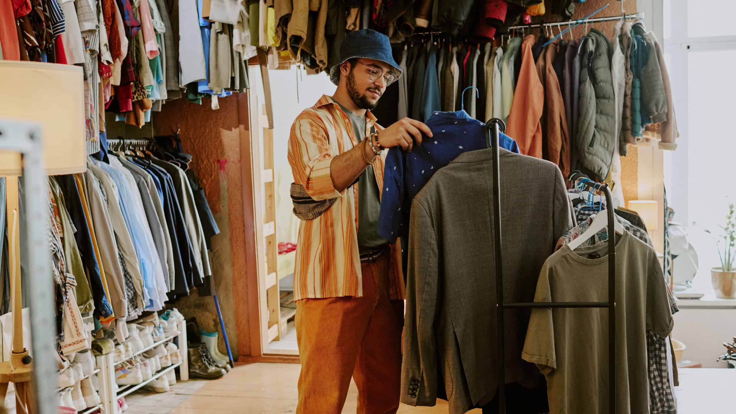 Person browsing clothes in a cozy vintage thrift shop filled with various garments and accessories hanging on racks