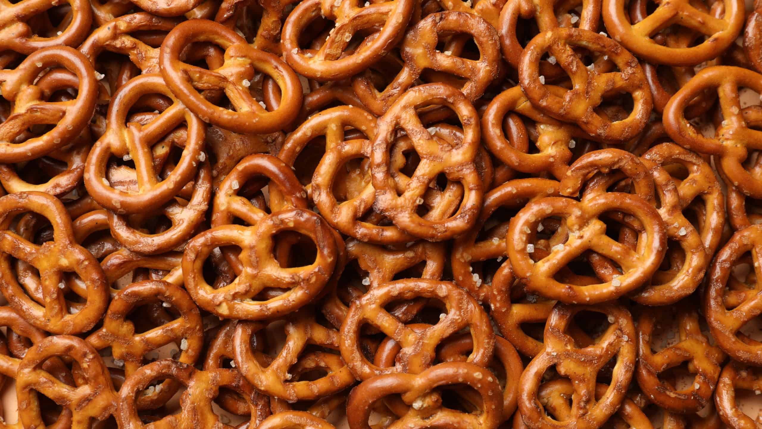 Many delicious pretzel crackers as background, top view