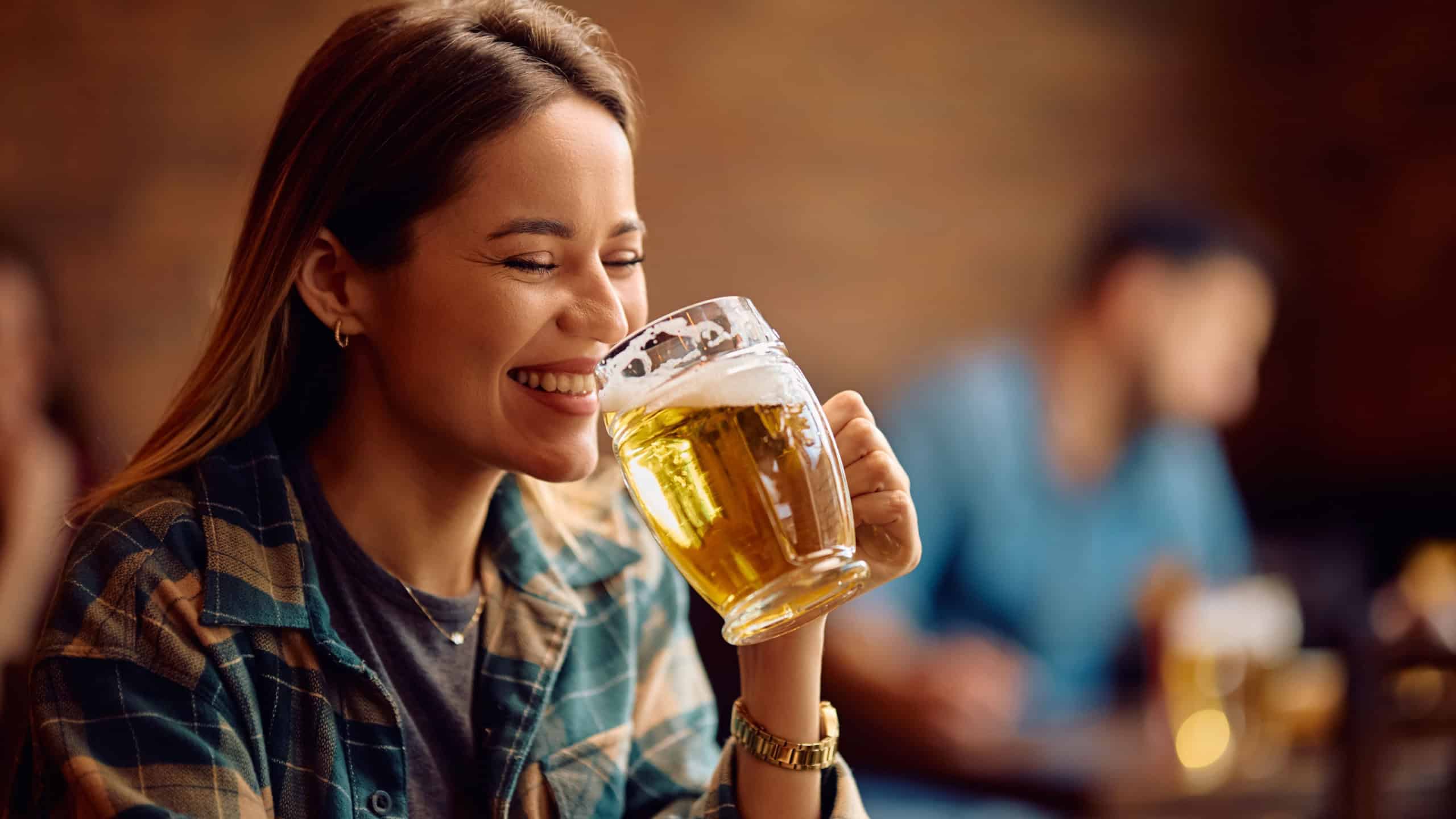 Three glasses of chilled beer near beer cask on old wooden table and brick wall at the background. 