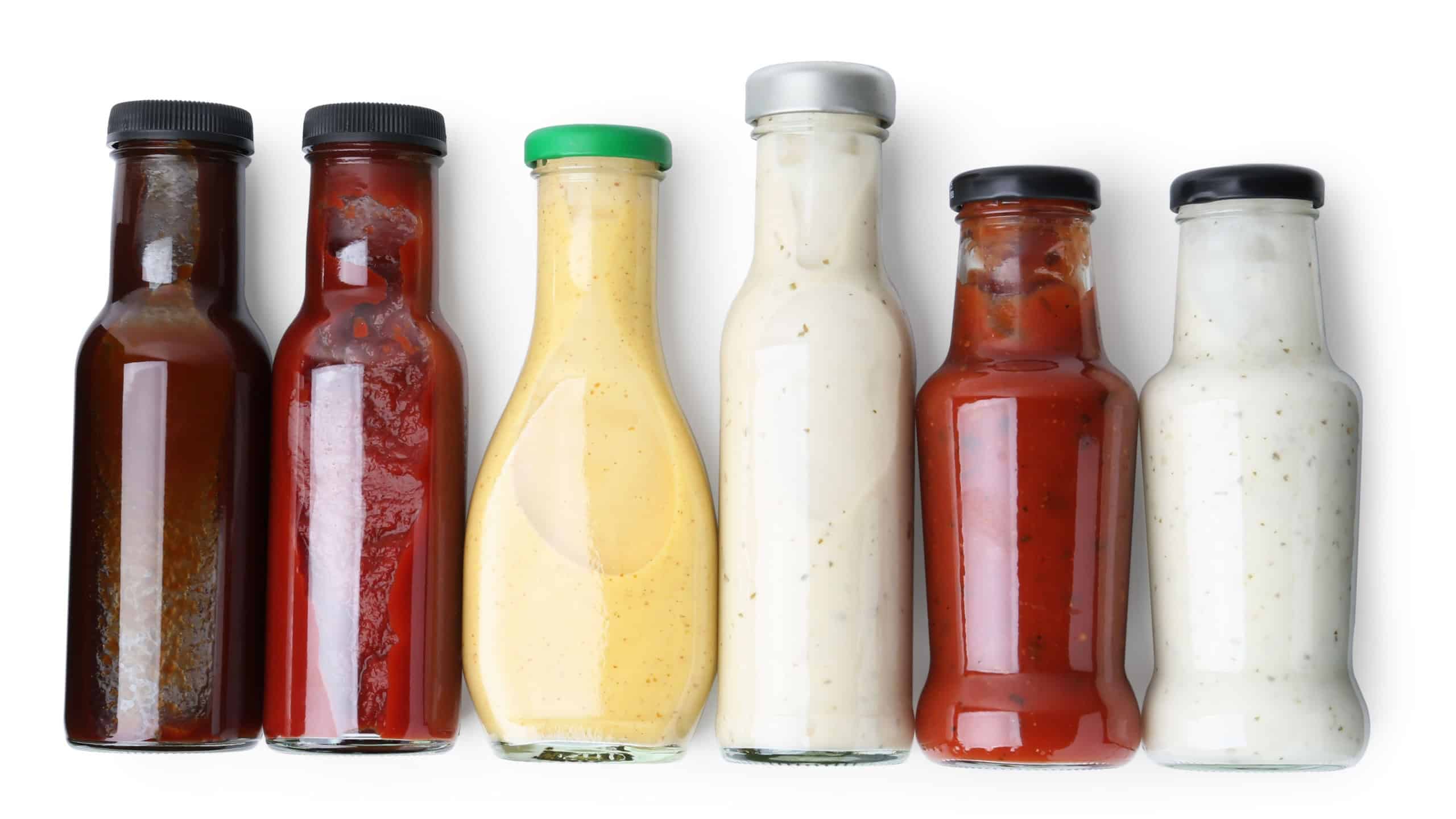 Different delicious sauces in glass bottles isolated on white, top view