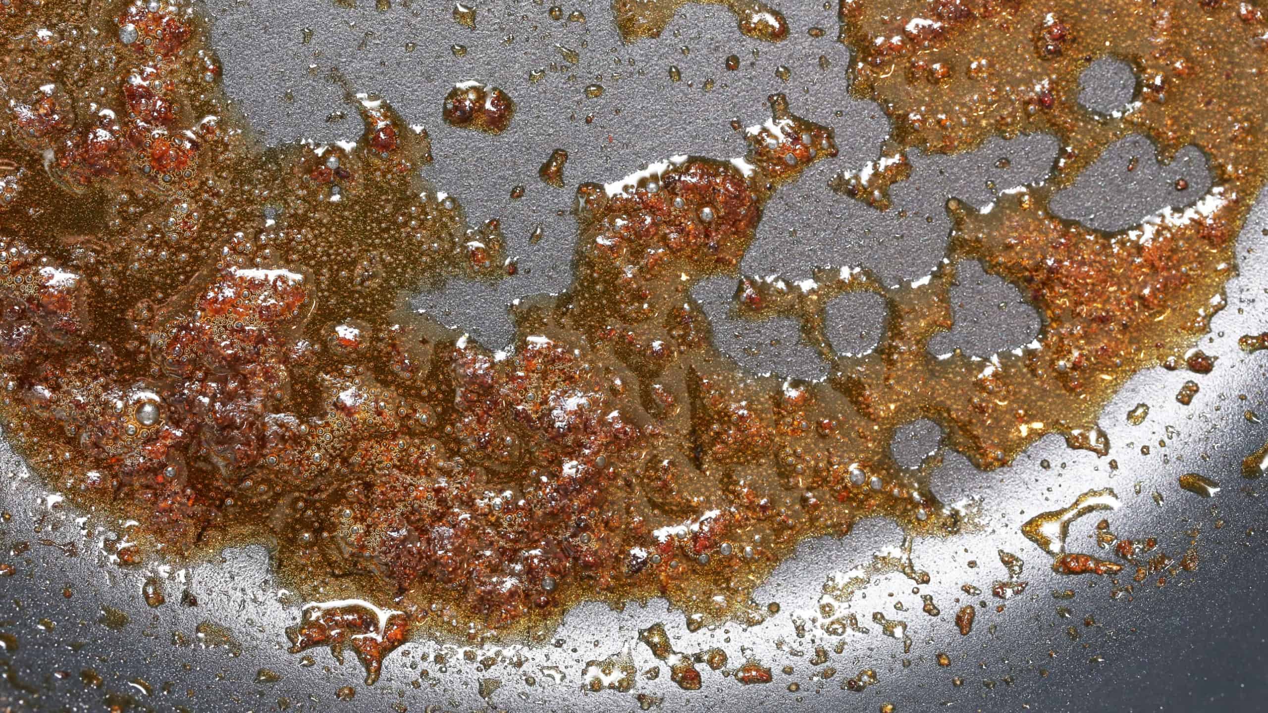 Old used oil on a frying pan. Burnt food residue and grease stains on a dirty non-stick surface. Cooking aftermath with leftover fat droplets. Kitchen wear and tear close-up. Dirty frying pan.
