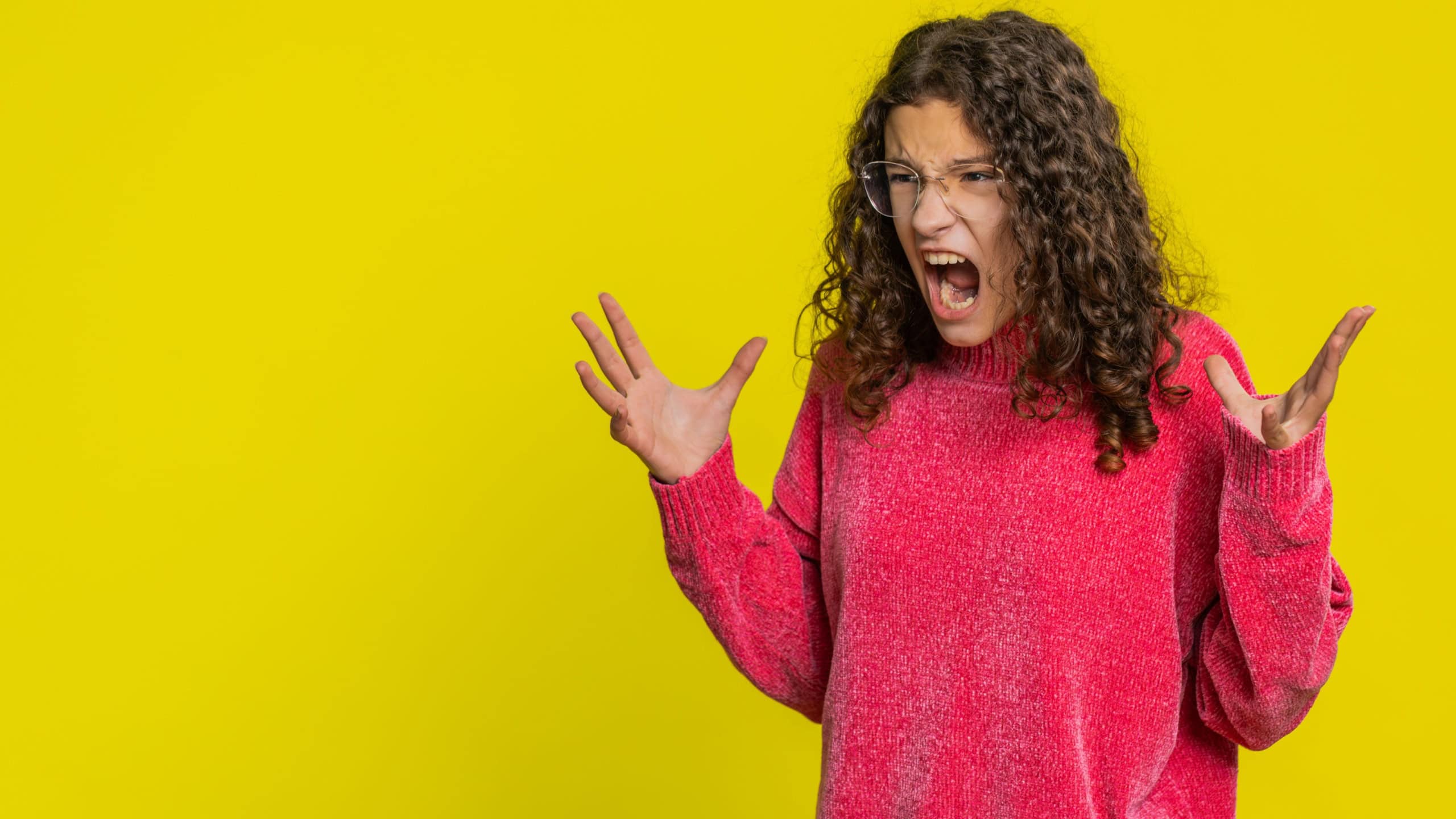Irritated angry Caucasian young teenager girl screams from stress tension problems feels horror hopelessness fear surprise shock expresses rage nervous, quarrel. Teen child kid on yellow background