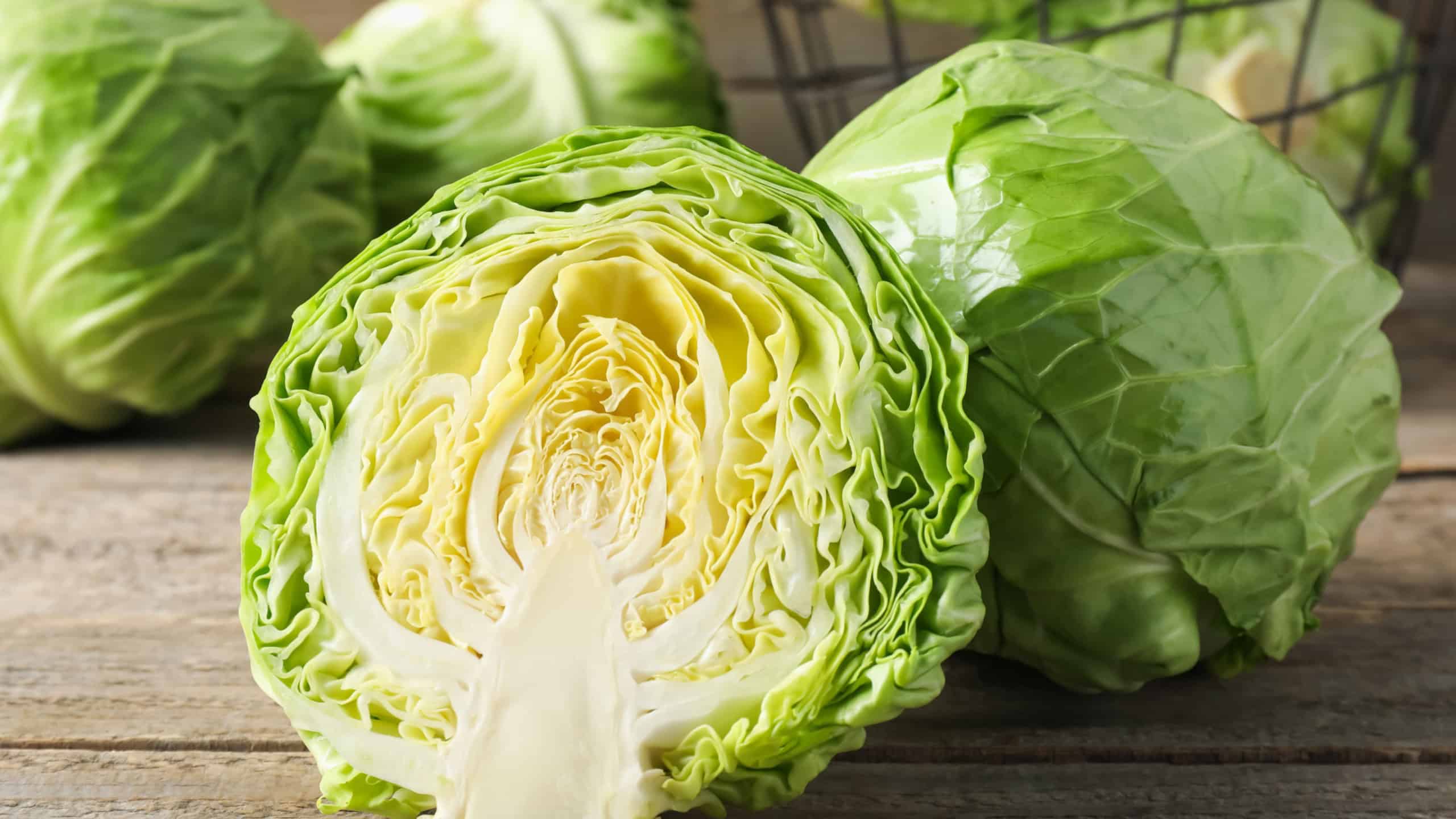 Fresh cabbages and basket on wooden table, closeup