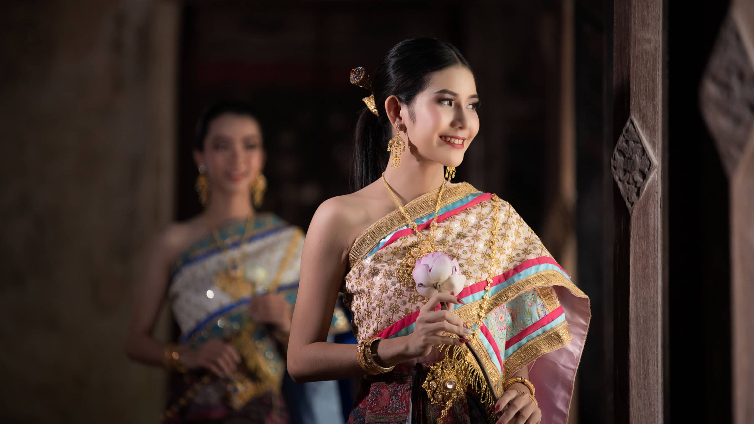 Women beautiful in traditional Thai attire delicate pink flower in her hand image evokes a sense of grace, heritage, and timeless beauty, showcasing traditions and fashion of Thai culture concept.