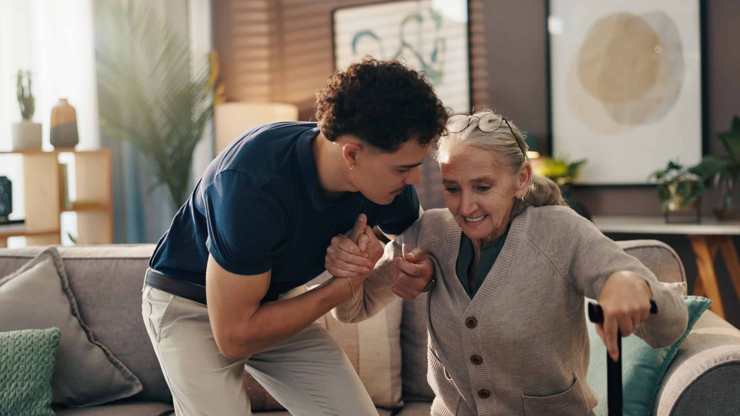 Senior woman, caregiver and help with walking stick on sofa for mobility, assistance and recovery. Health worker, elderly person and support with cane in assisted living for balance or rehabilitation