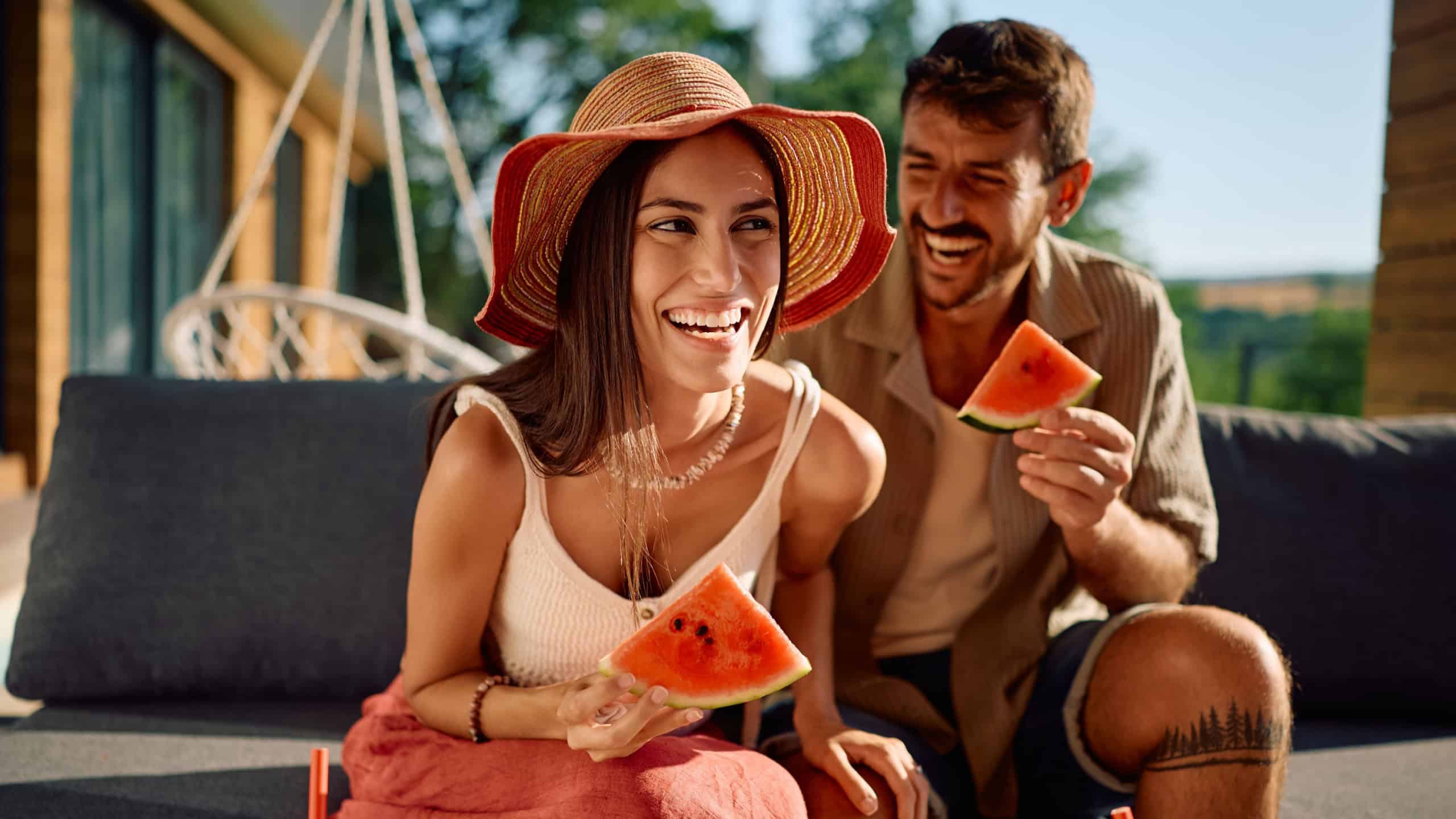 Cheerful woman and her boyfriend having fun while eating watermelon on a patio. 
