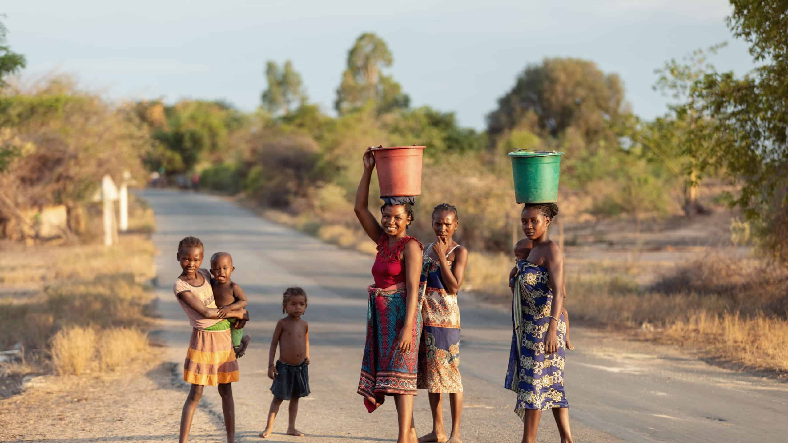Mahabo, Madagascar - November 3 2022: Malagasy women carrying buckets of water on their heads on a rural road, portraying traditional life in Menabe region.