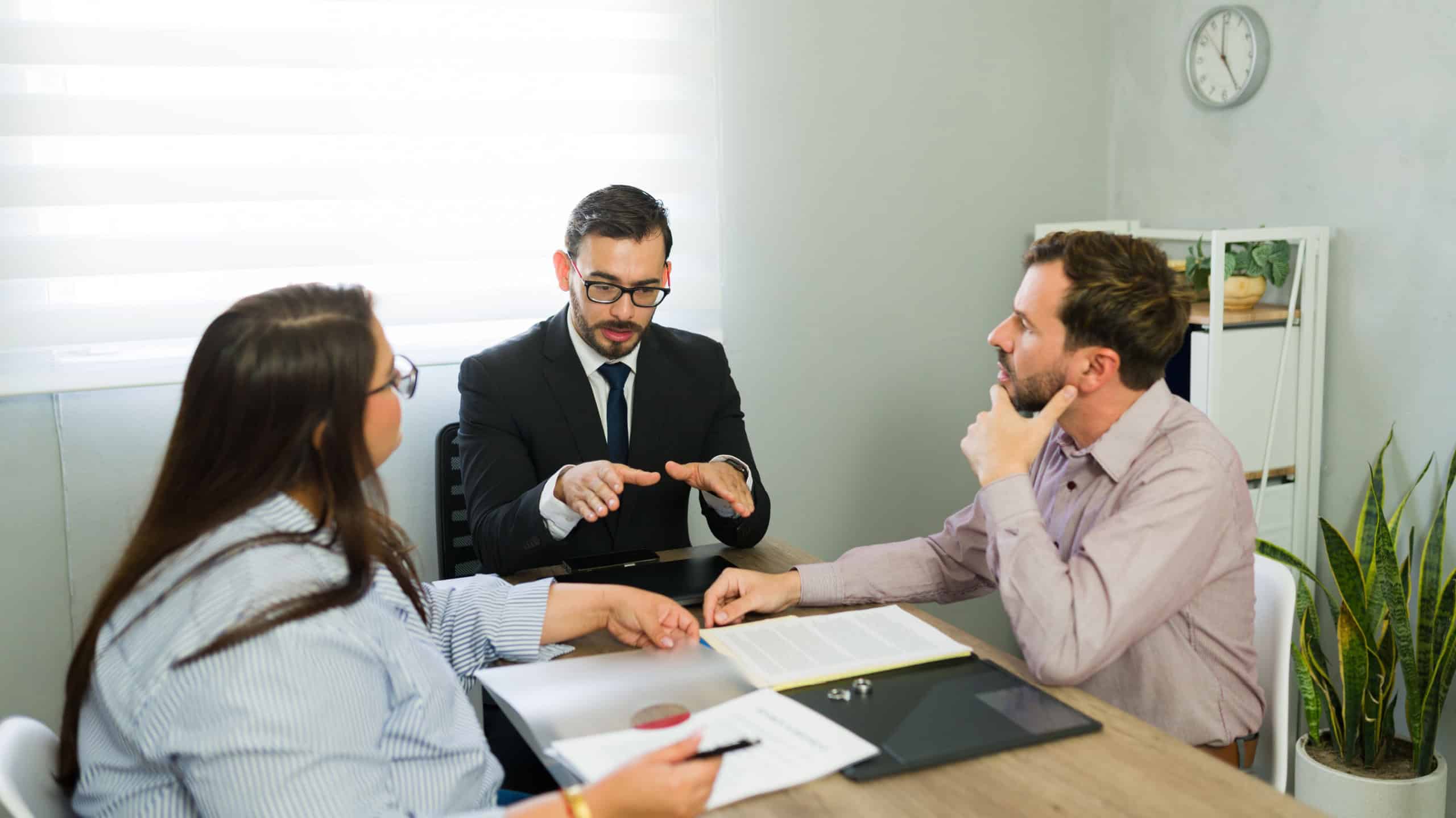 Attorney mediating between a distressed couple, reviewing legal documents and discussing separation terms at an office meeting