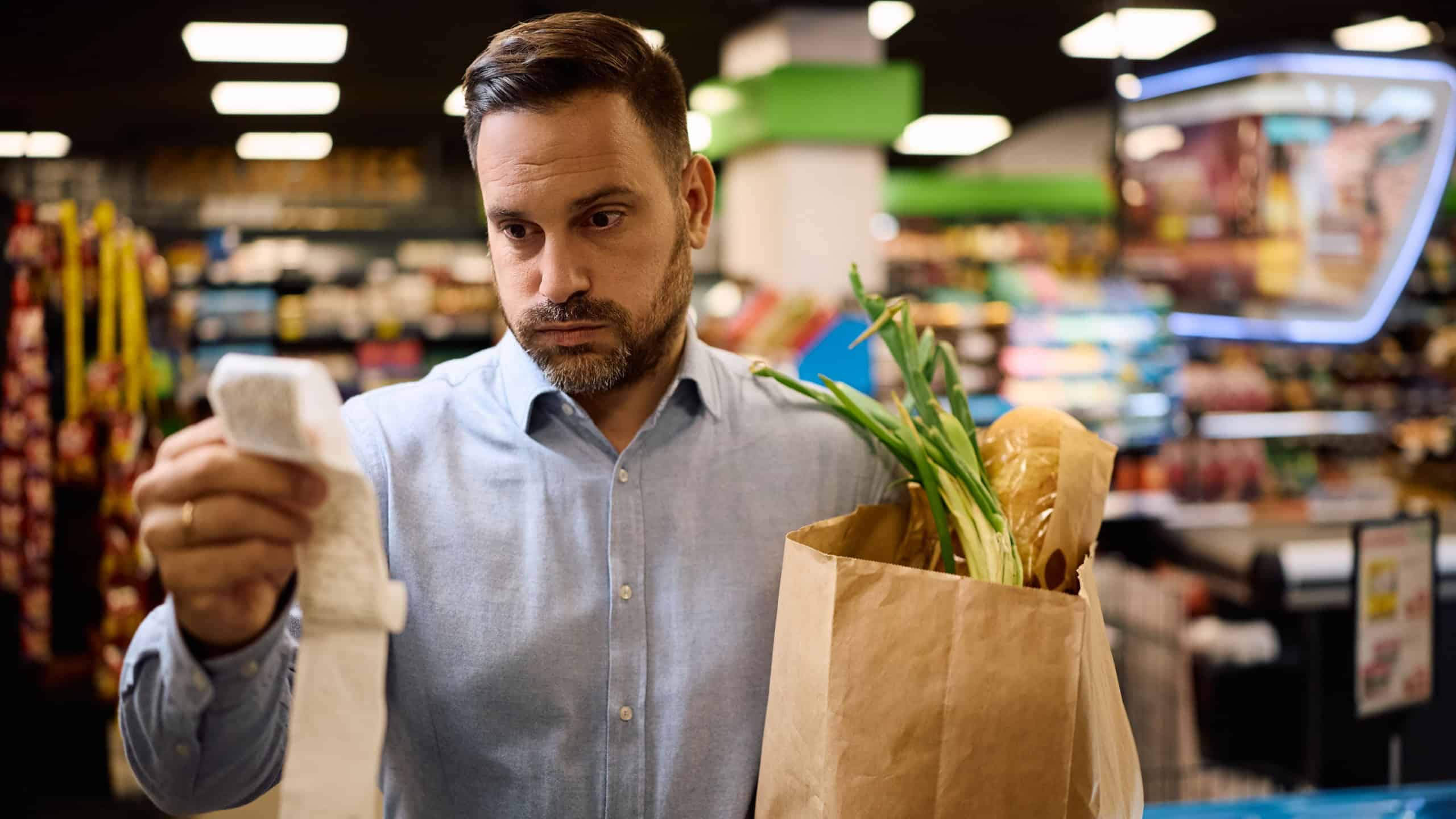 Worried man checking the bill after buying groceries at supermarket.
