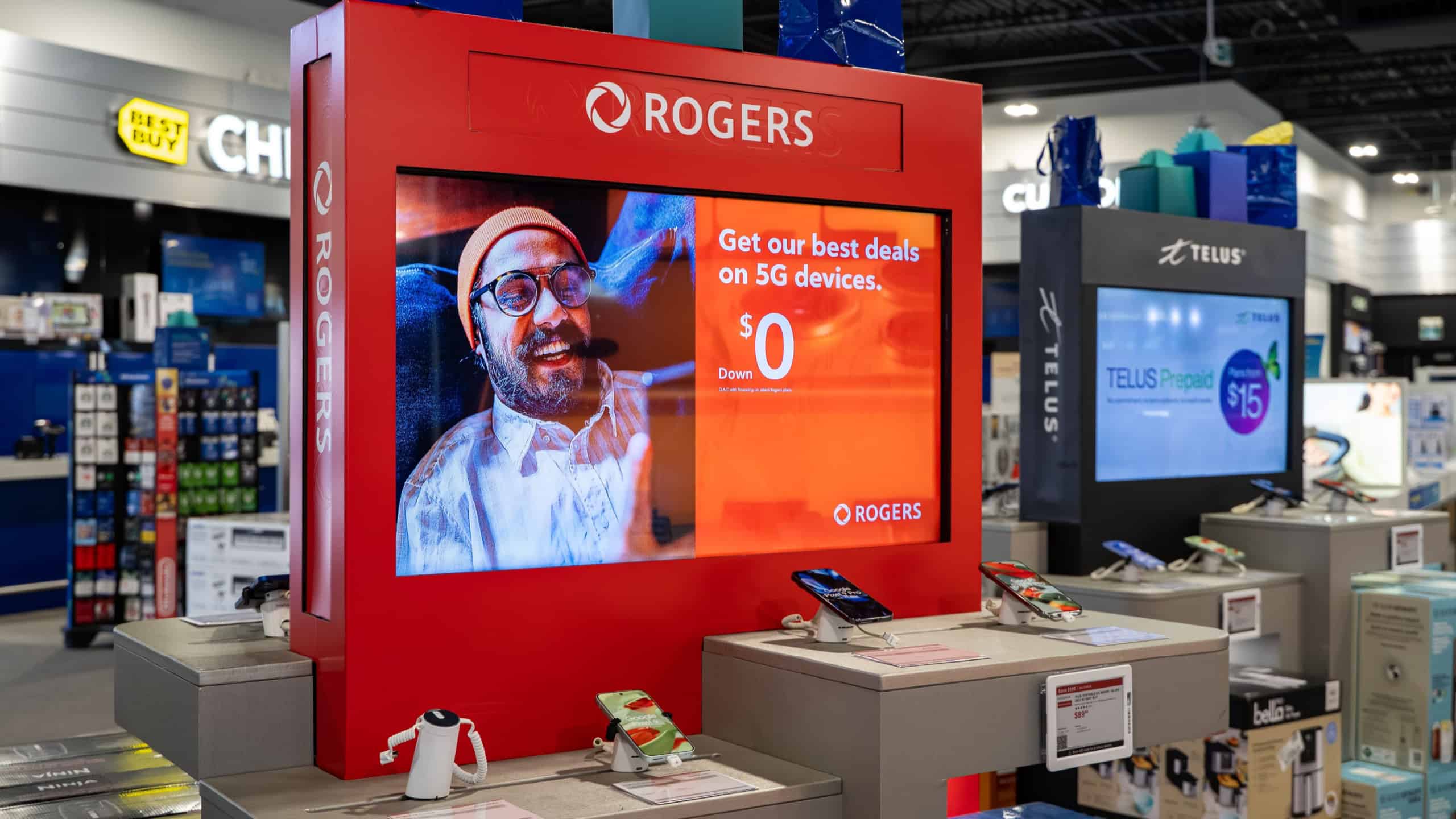Interior view of retail display with Rogers promotional screen and mobile devices. Toronto, Canada - December 3, 2025.
