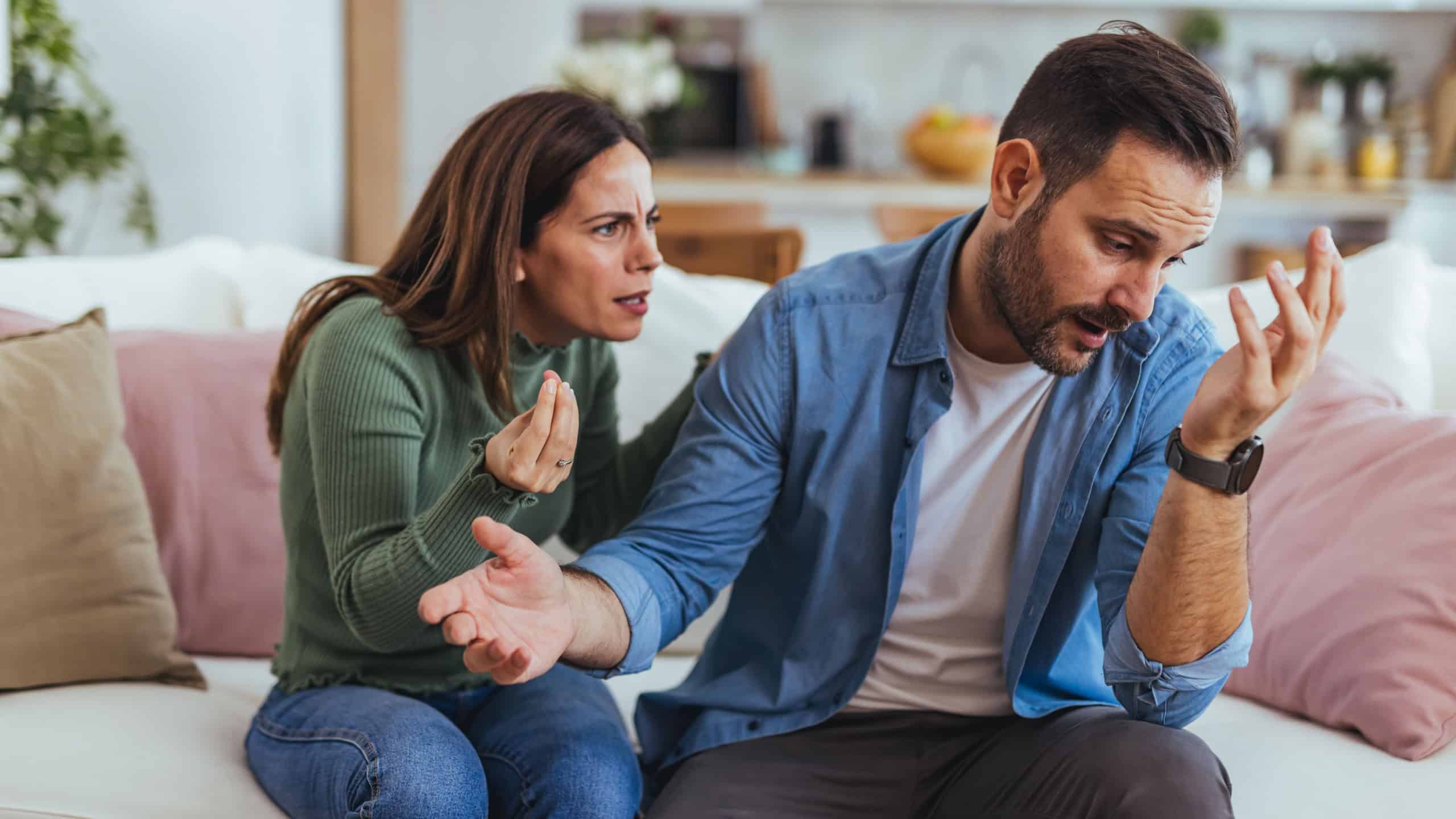 Frustrated couple arguing on a living room sofa, showing tension, emotional strain and miscommunication during a domestic disagreement. Useful for themes of relationship problems, counseling, stress and couples therapy.