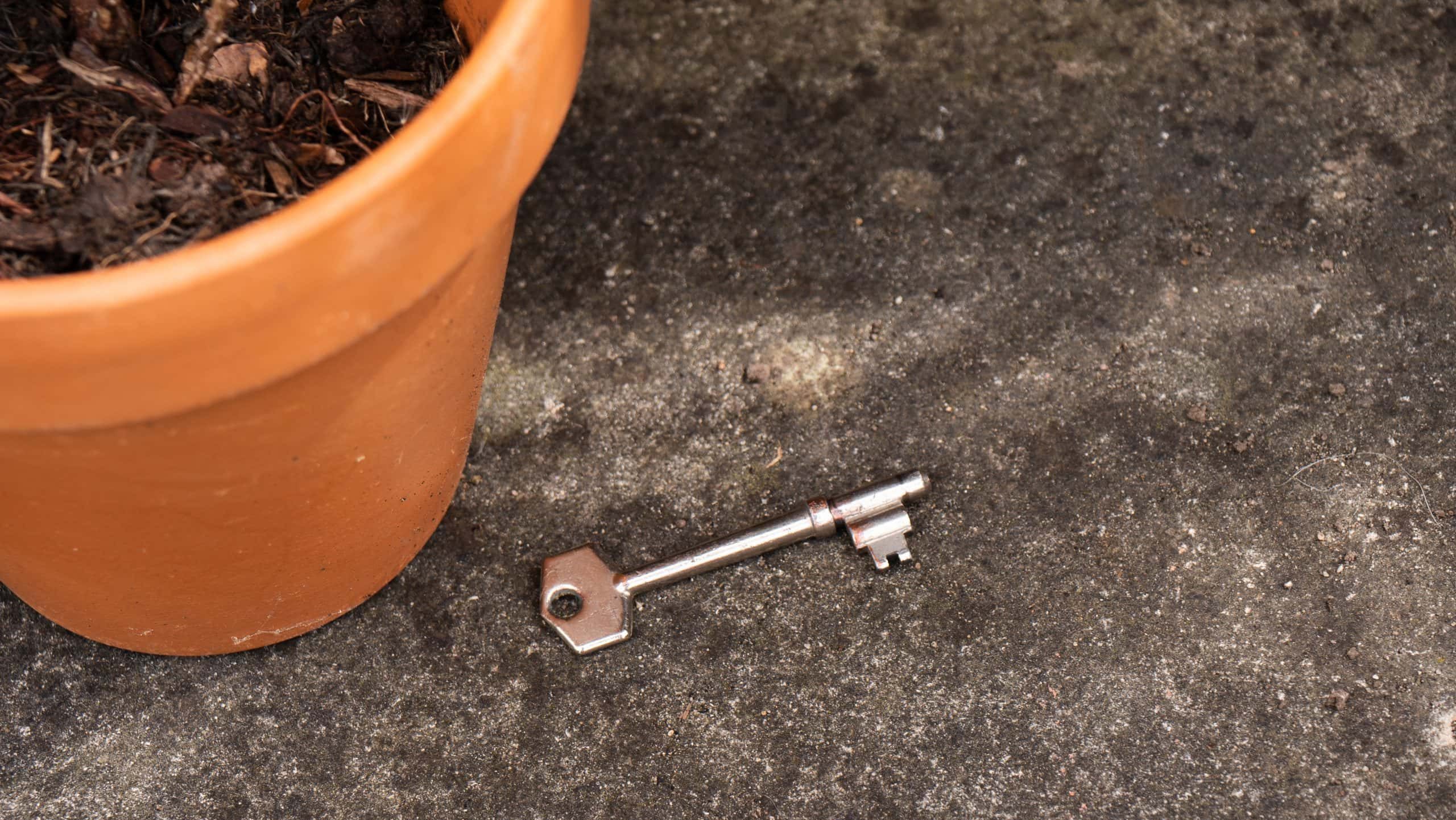 Door key near plant pot outside of home medium shot selective focus