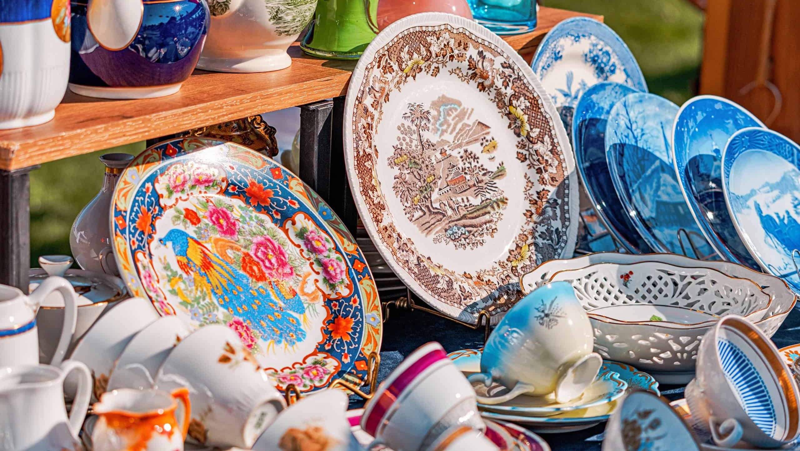 1 June 2025, Belgrade, Serbia: Colorful vintage porcelain cups, plates, teapots and vases displayed on a wooden stall at a flea market