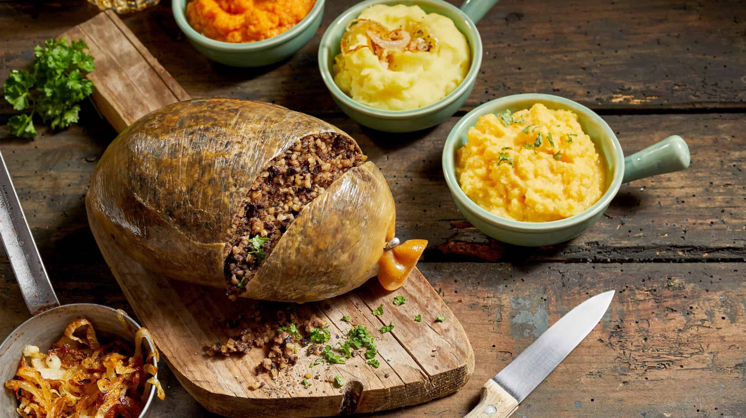 Traditional haggis meal for Robert Burns Supper, a Scottish tradition with cooked sliced haggis, neeps, tatties, onion and carrot on a rustic table