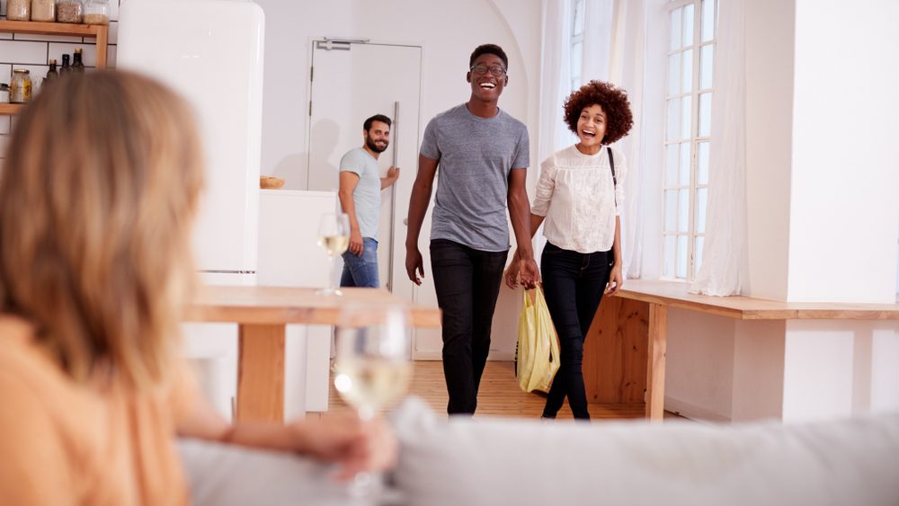 Couple Greeting Friends Arriving For Dinner Party At Home