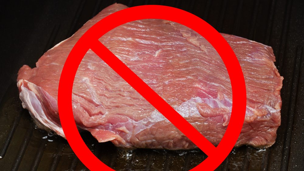 Healthy nutrition, diet and vegetarianism. Red prohibitory sign on a piece of meat, fried in a pan
