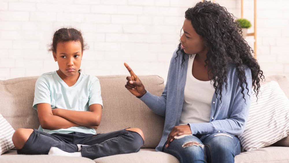 Family Discipline Concept. Grumpy black mom scolding her naughty little daughter on sofa at home