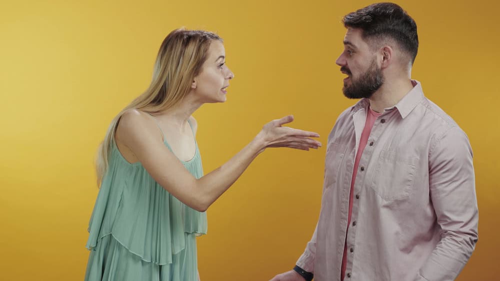 Furious young family couple arguing yelling words getting angry isolated on background. Offended man and woman using their smartphones turning back to each other.