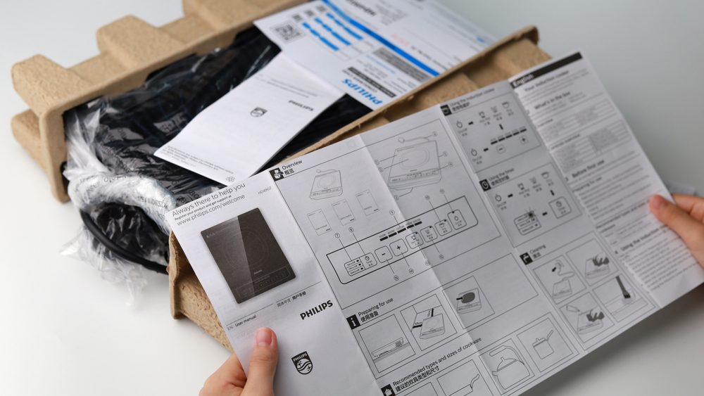 Lady’s hand pointing at the user manual of the brand new Philip induction stove during the open box.
